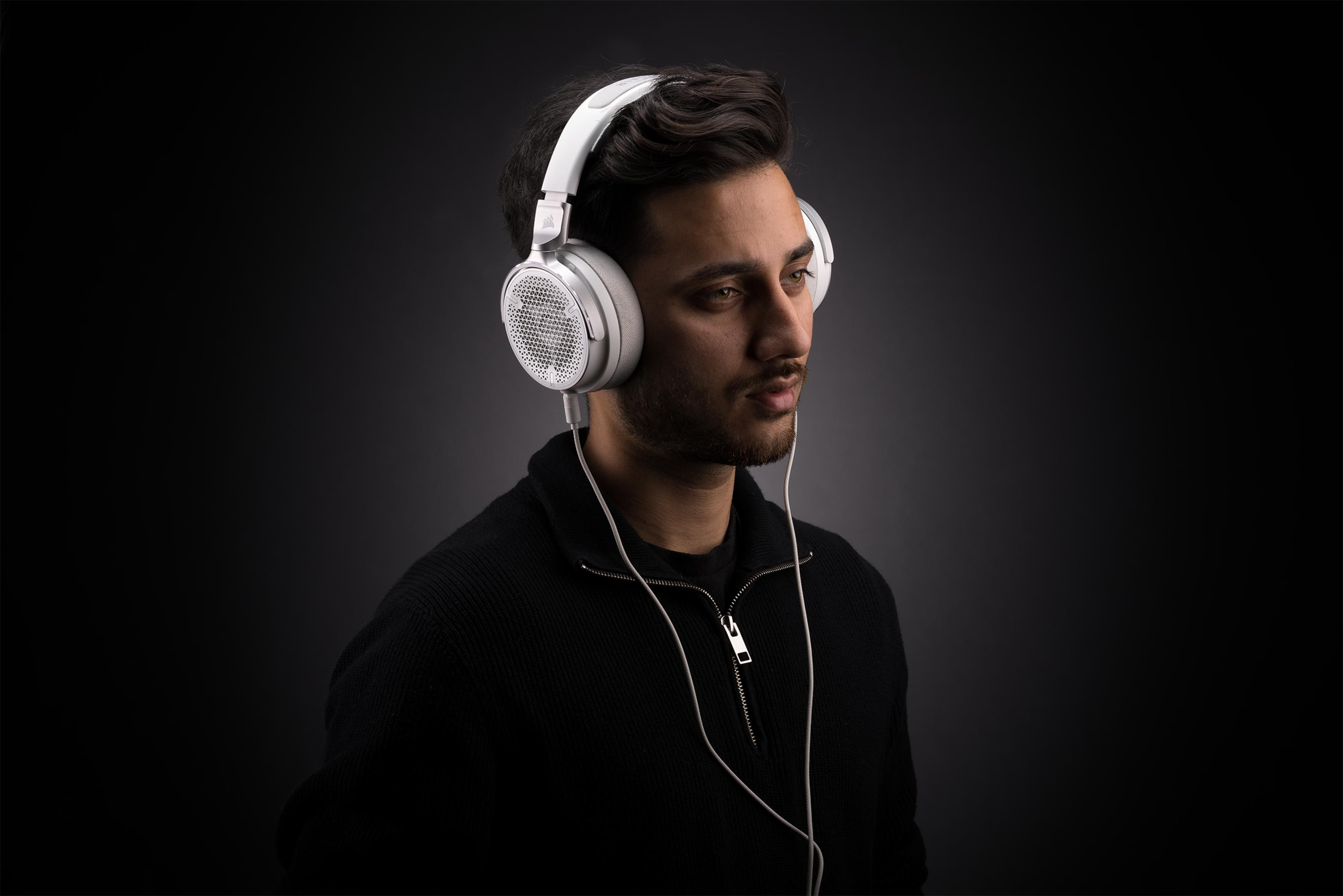 Mężczyzna w białych słuchawkach i czarnym swetrze na ciemnym tle.