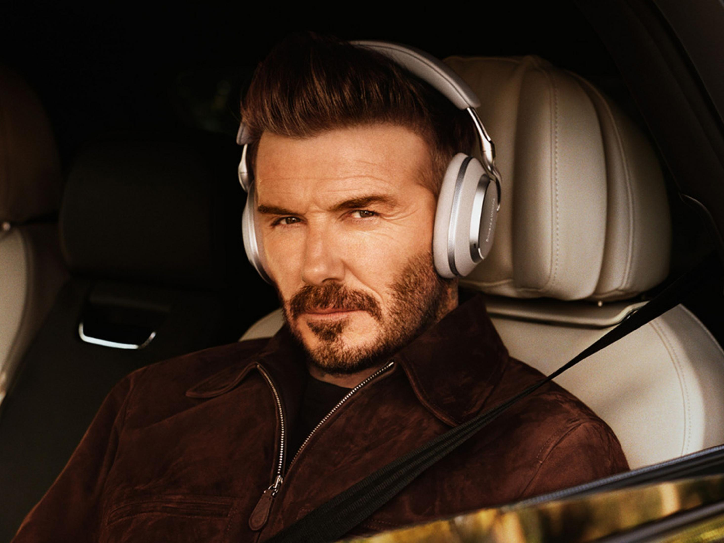 Uomo con cuffie in auto, giacca marrone, sedili beige.