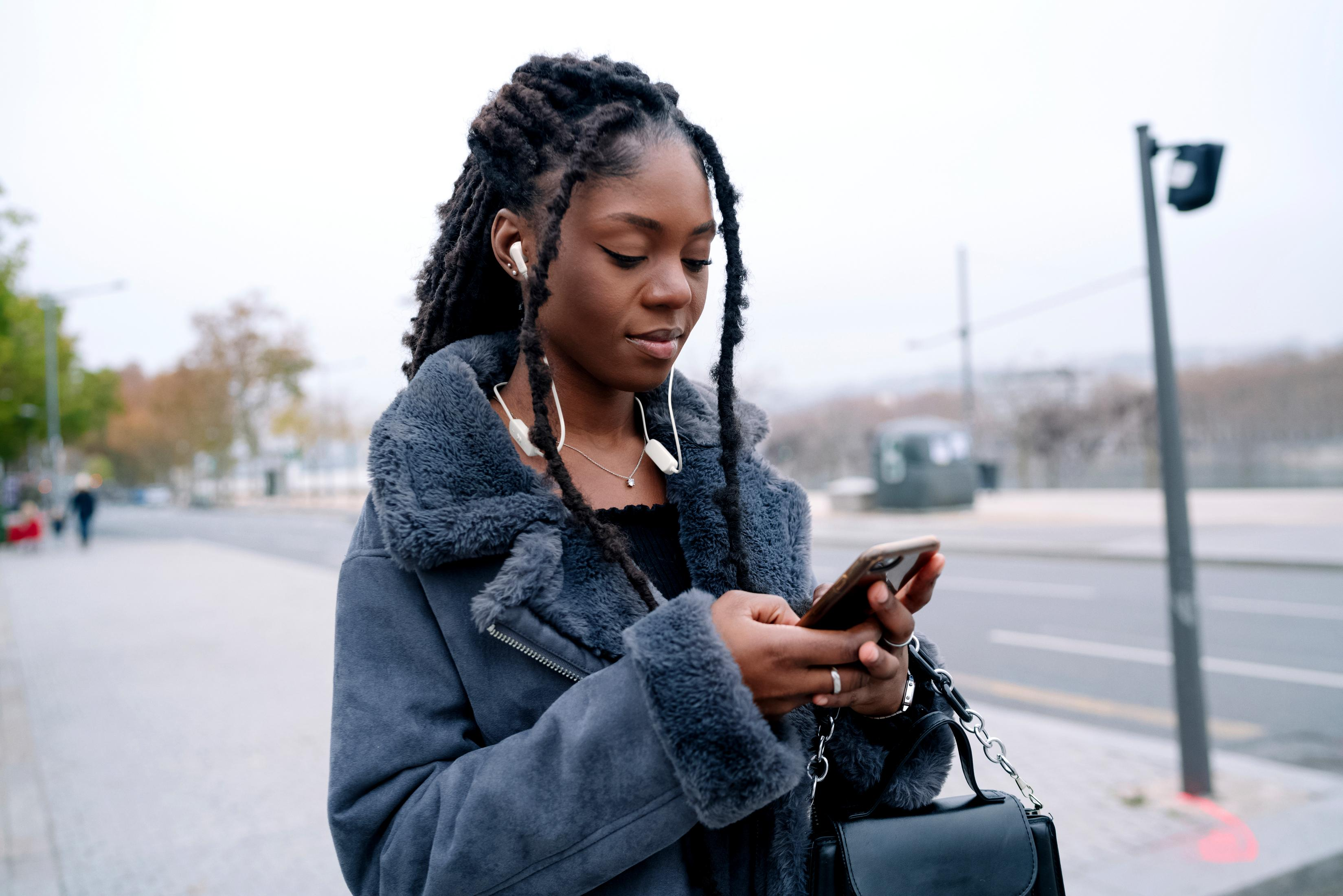 Een vrouw met dreadlocks in een grijze jas gebruikt haar telefoon.