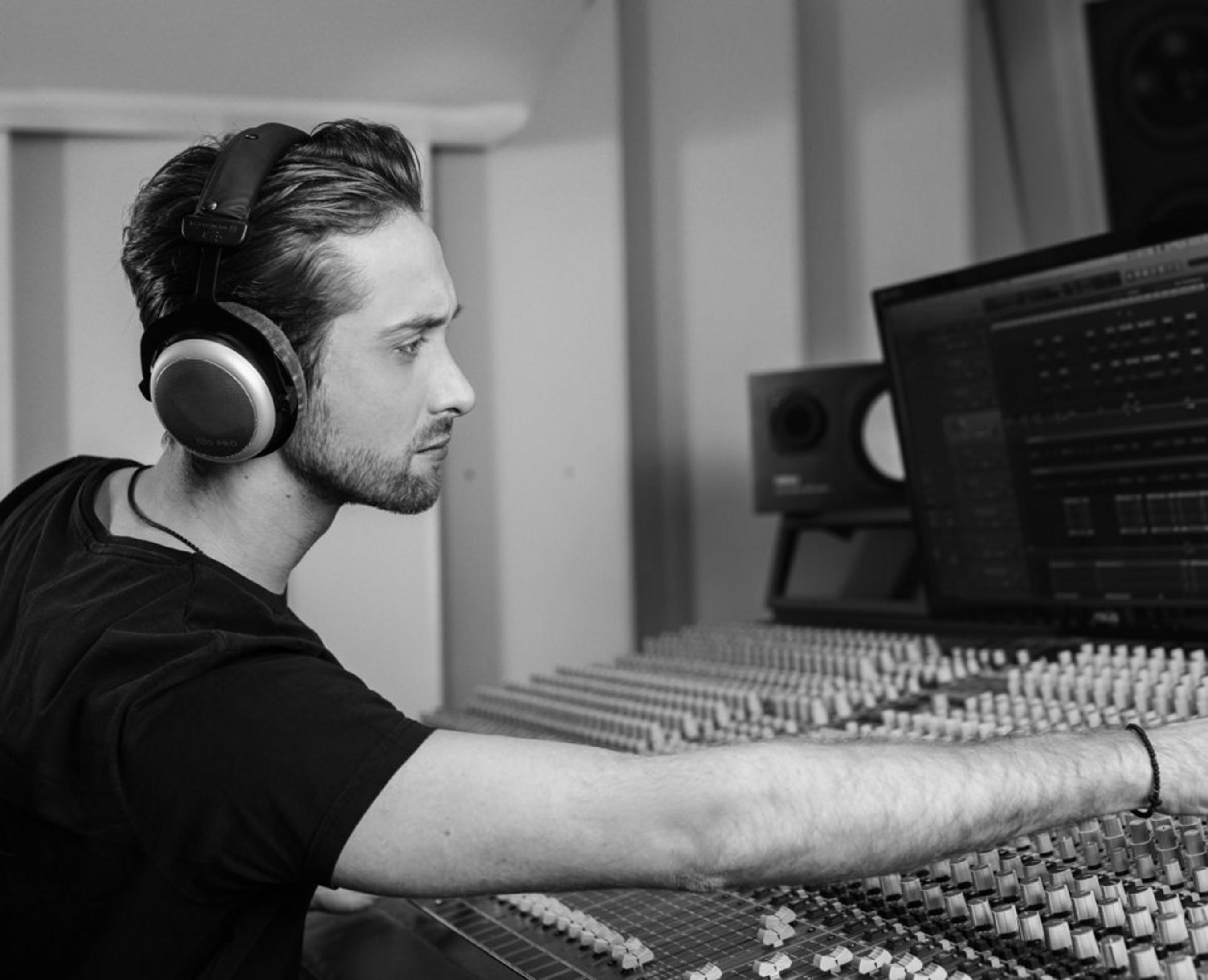 Mężczyzna w słuchawkach przy konsolecie mikserskiej, produkcja muzyczna w studio.