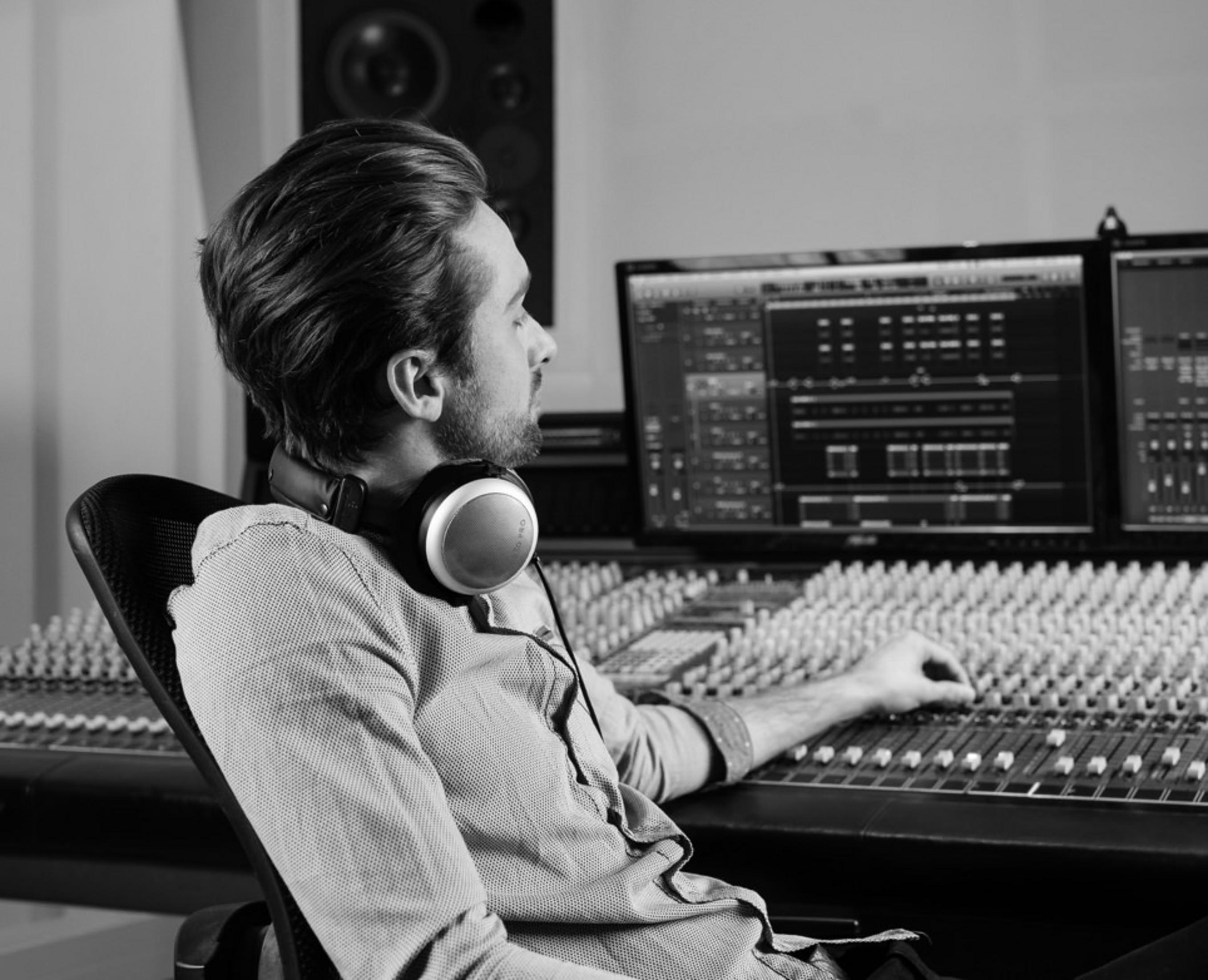 Mężczyzna w słuchawkach siedzi przy konsolecie mikserskiej w studiu.