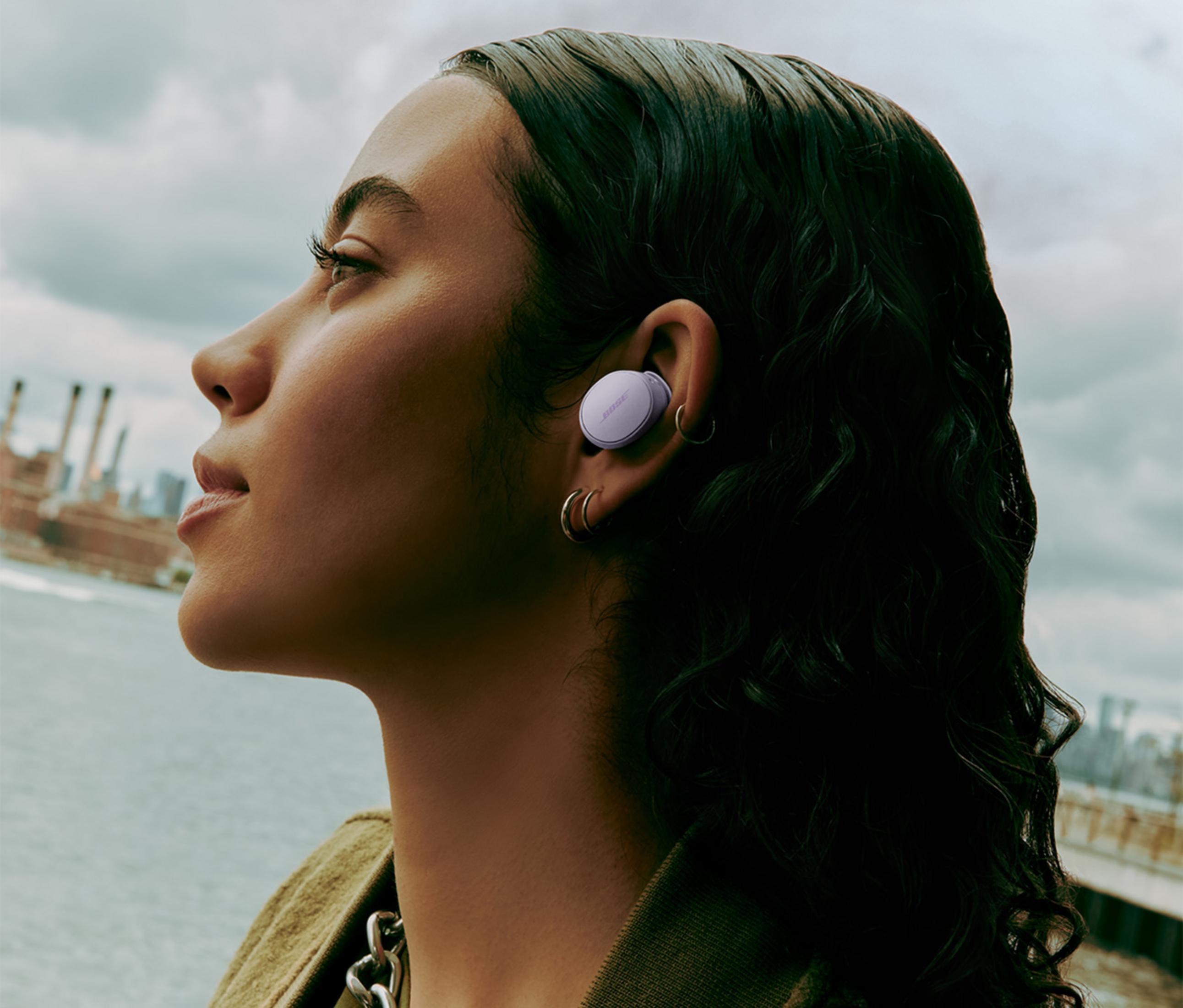 Kobieta ze słuchawką w uchu, na tle budynków przemysłowych.