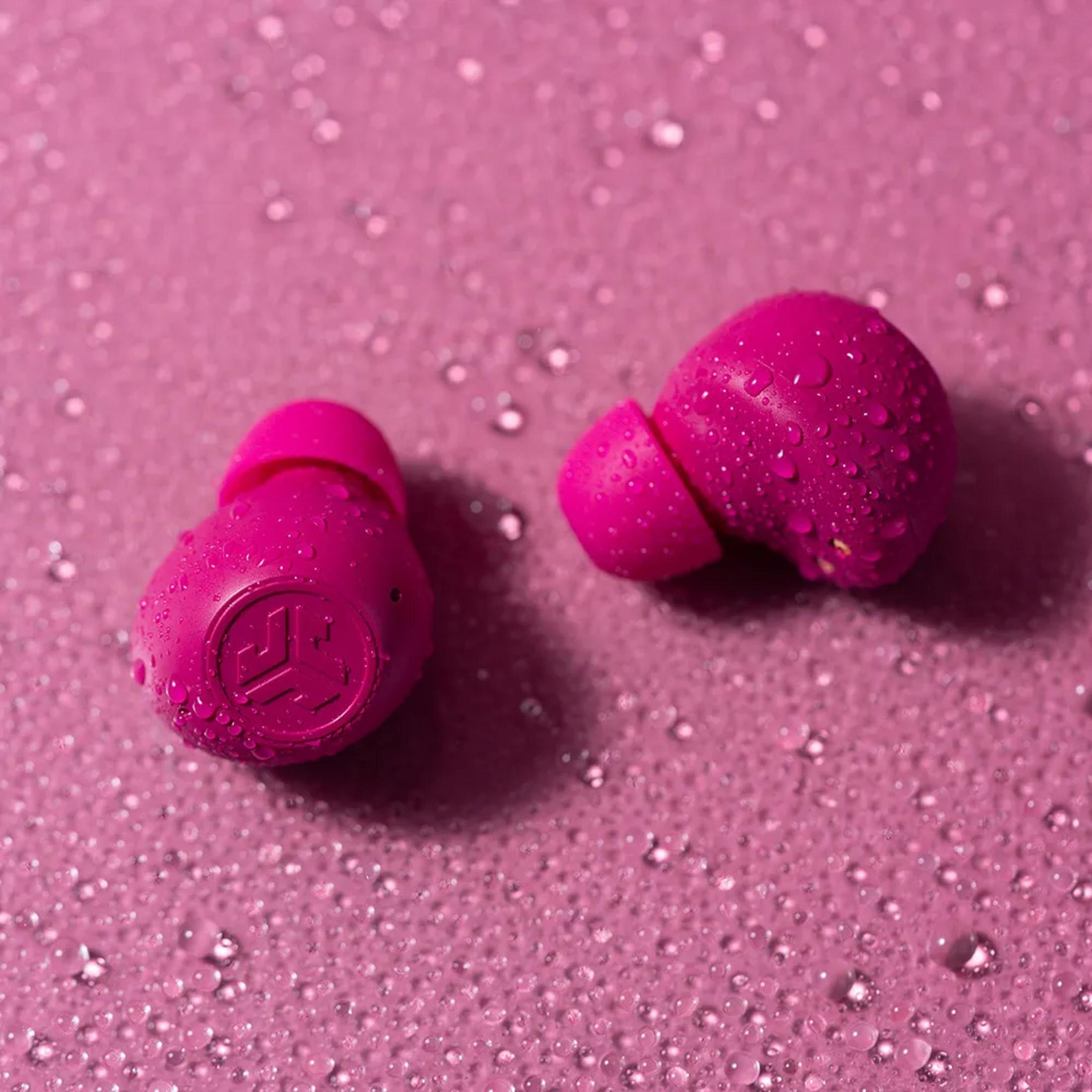 Dwa różowe słuchawki bezprzewodowe z kroplami wody na różowej powierzchni.