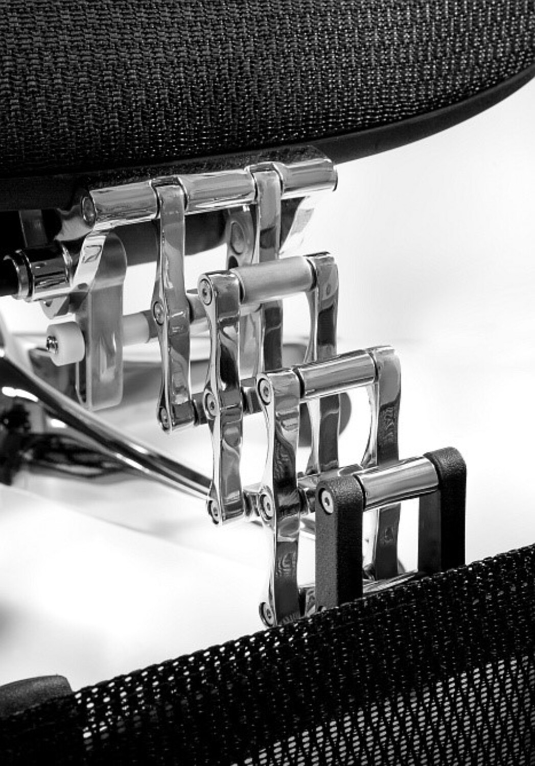 Chromowane dźwignie i czarna siatka krzesła.