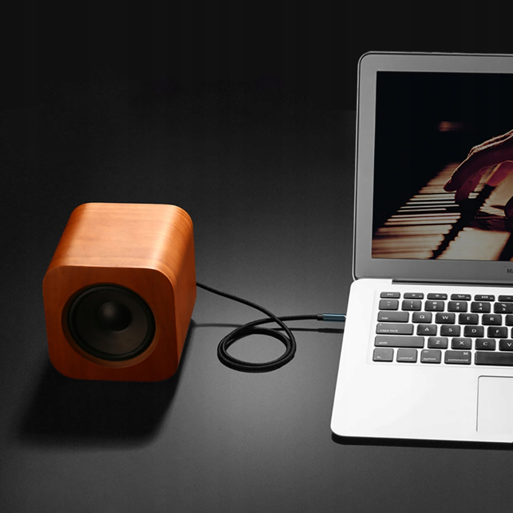 Drewniany głośnik podłączony kablem do laptopa wyświetlającego klawisze fortepianu.