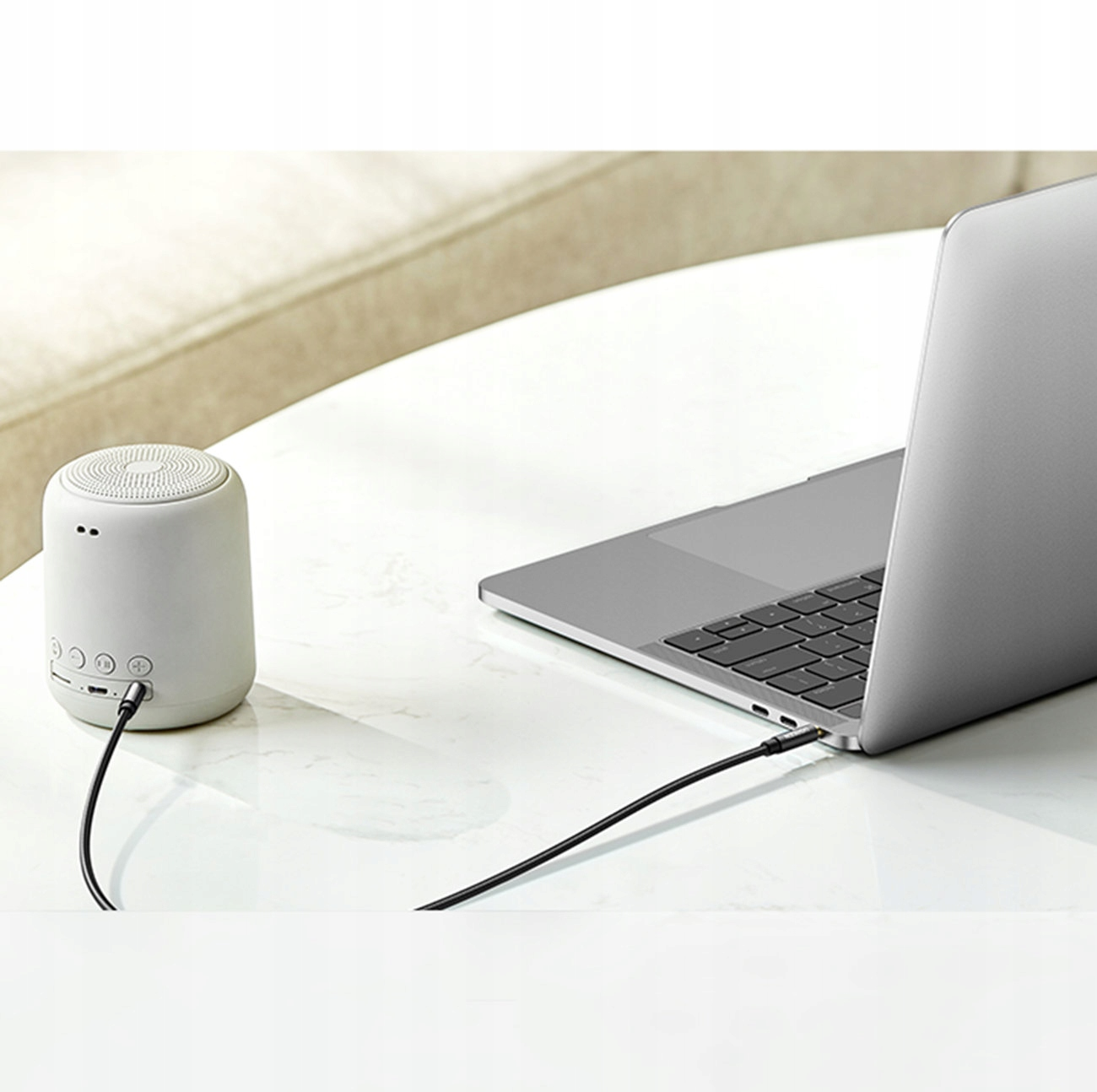 Biały głośnik jest podłączony do laptopa czarnym kablem.