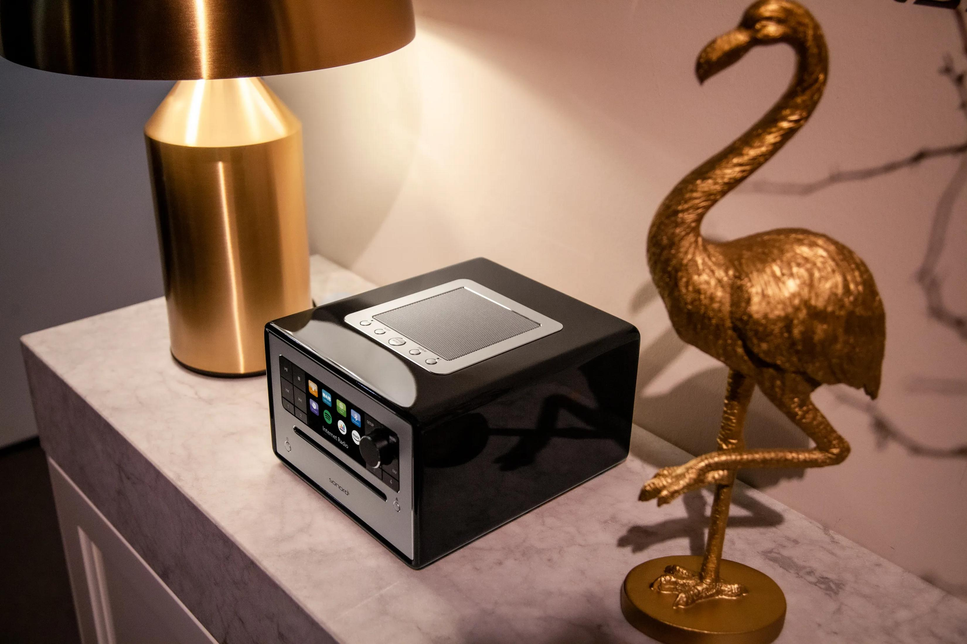 Een gouden flamingo naast een zwarte radio op een marmeren tafel.