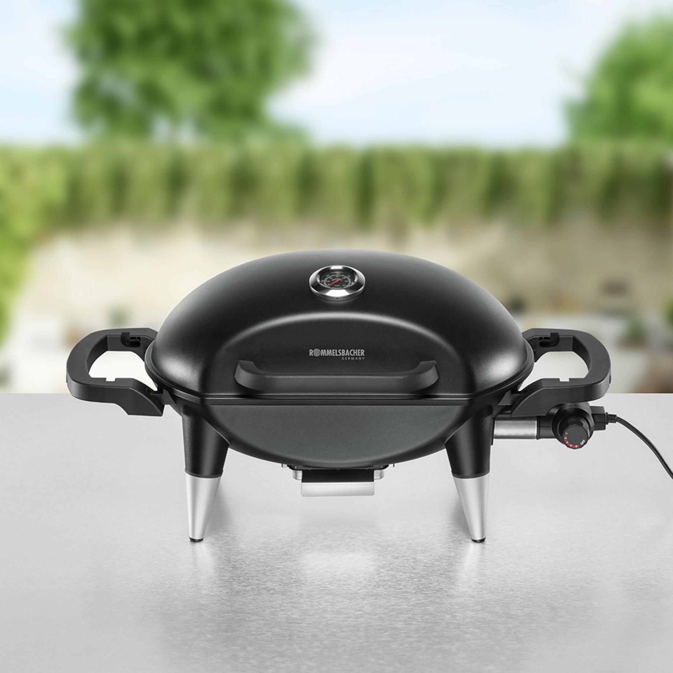 Black electric grill with thermometer on table, outdoors.