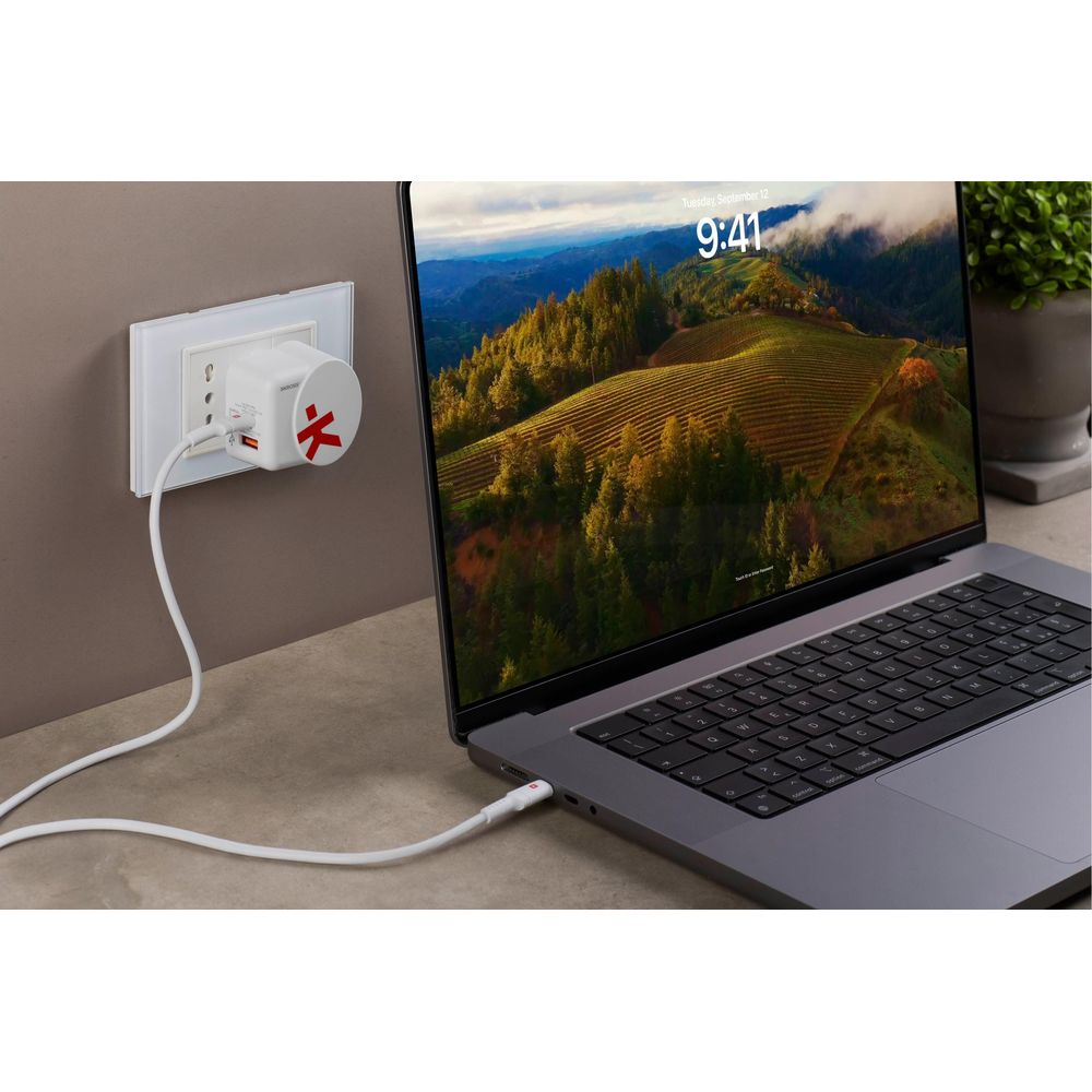 Un adattatore da viaggio bianco con simbolo rosso carica un laptop.