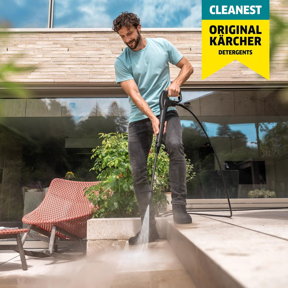 Uomo lava gradini con idropulitrice davanti casa moderna, logo Karcher giallo.