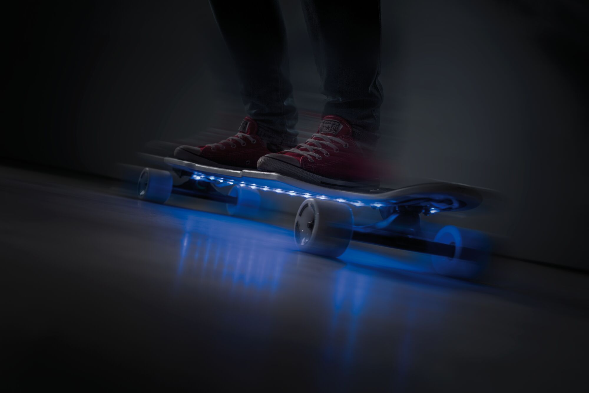 Ein Skateboard mit blauen LEDs fährt auf einem dunklen Boden.
