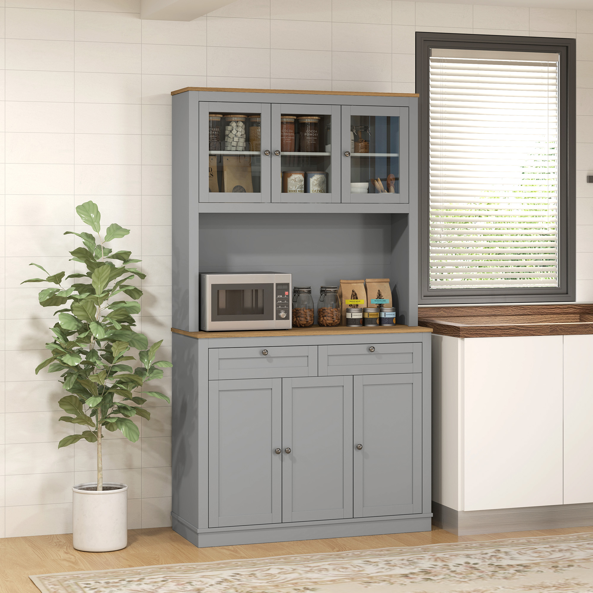 Un aparador de cocina gris con gabinetes de vidrio, un microondas y frascos decorativos, junto a una ventana grande con persianas.