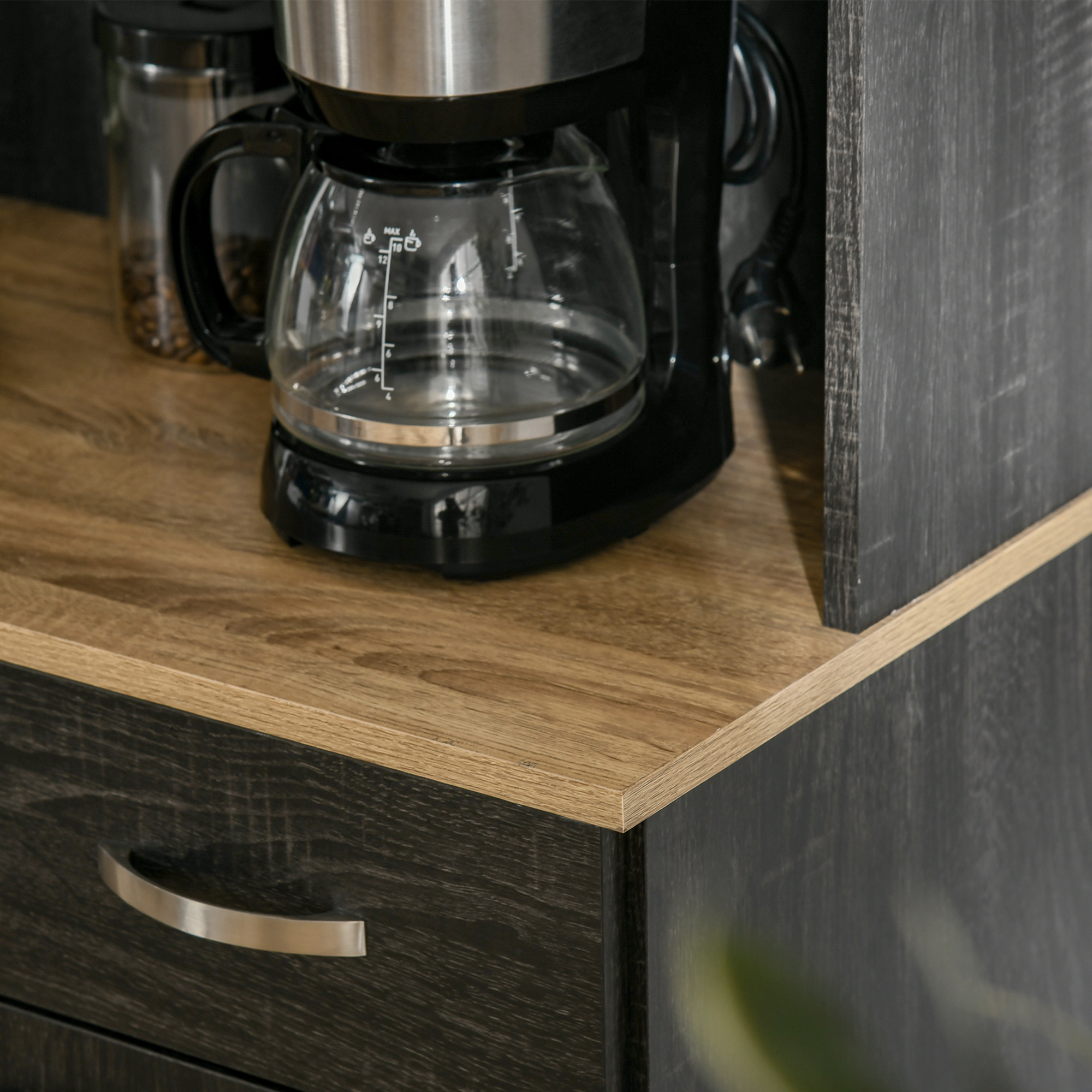 Cafetera con jarra de cristal sobre superficie de madera, junto a un recipiente de cristal con granos.