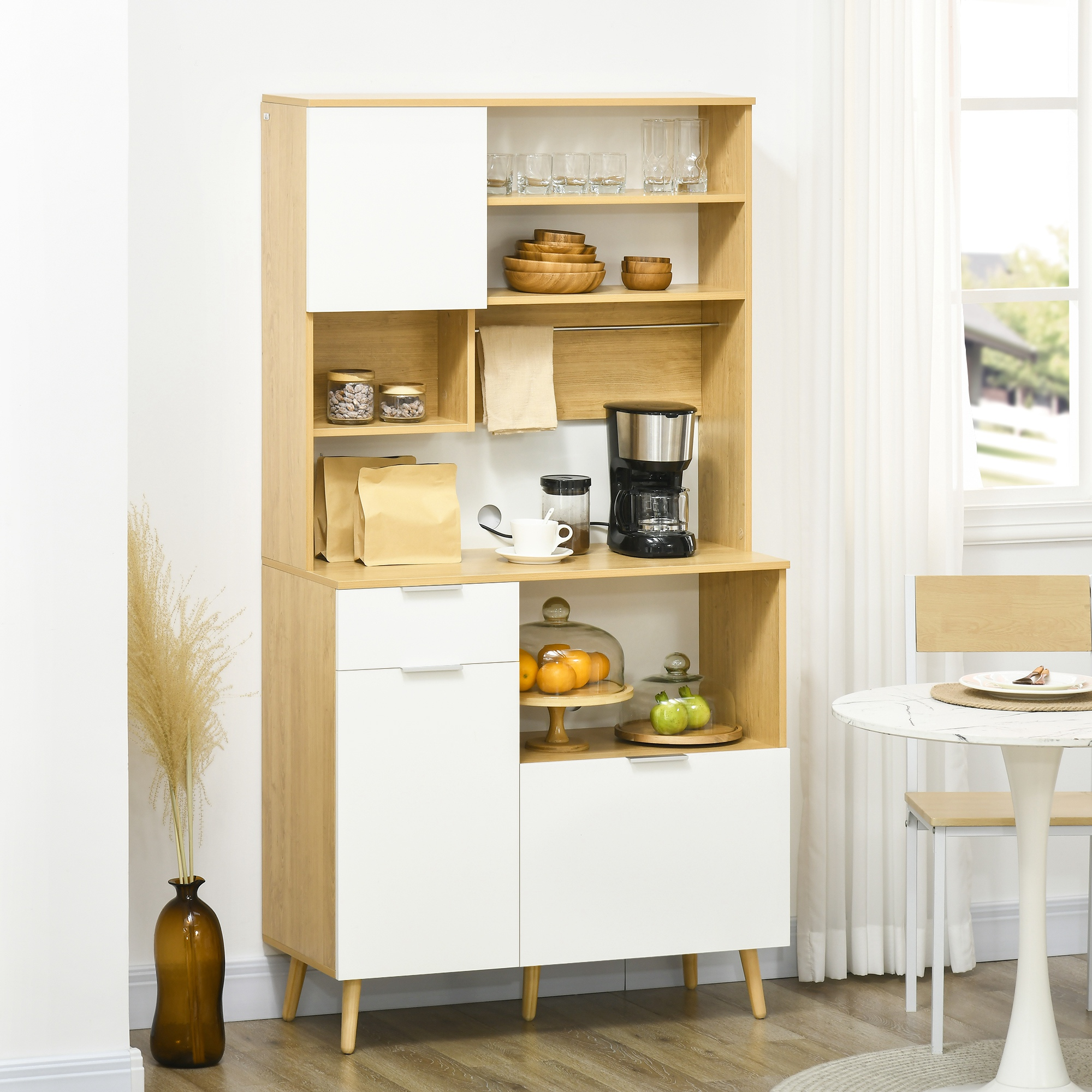 Un aparador de cocina funcional con puertas blancas, detalles de madera, vasos, cuencos, cafetera y fruta.