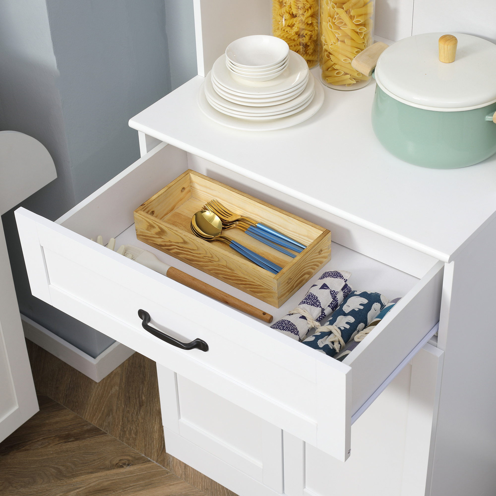 Cajón abierto con cubiertos dorados, mangos azules y paños de cocina.