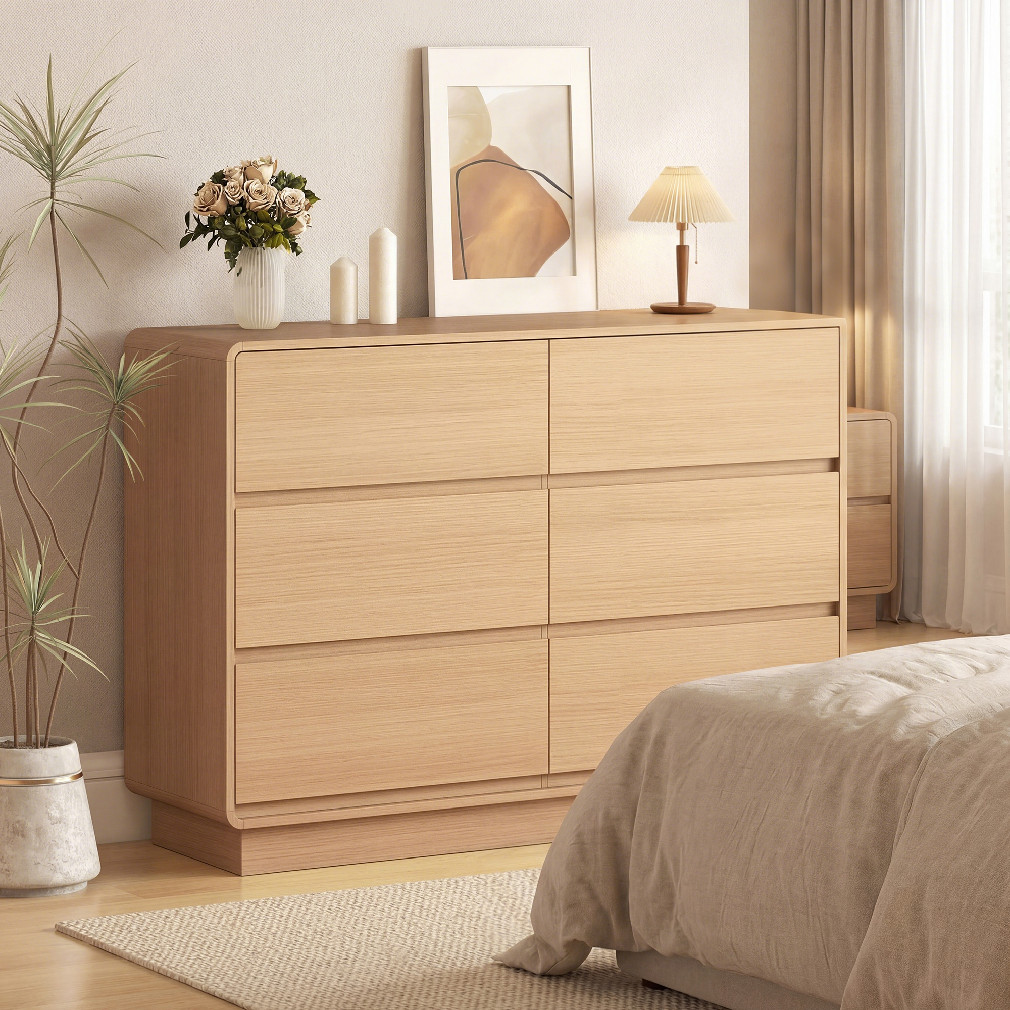 Cómoda de madera clara con seis cajones, jarrón con flores, velas y lámpara.