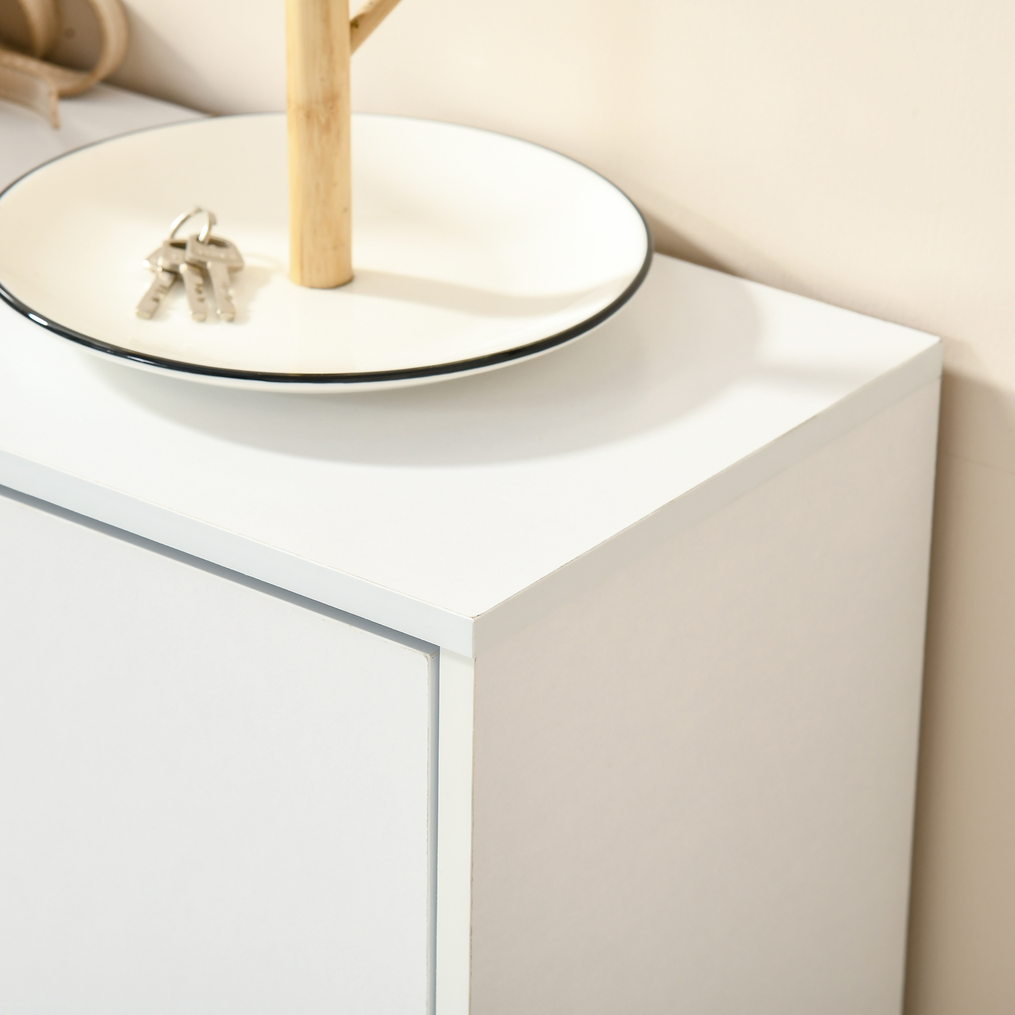 Un cuenco blanco con tres llaves y un gancho de madera sobre un mueble blanco.