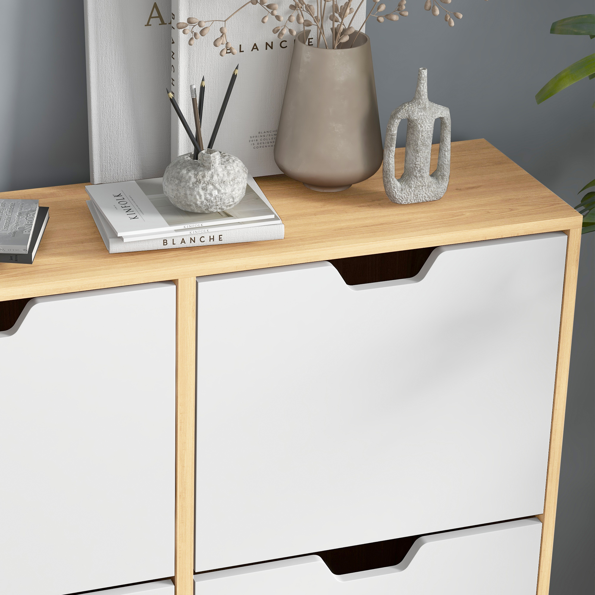 Superficie de madera con cajones blancos, libros, jarrones y lápices como decoración.