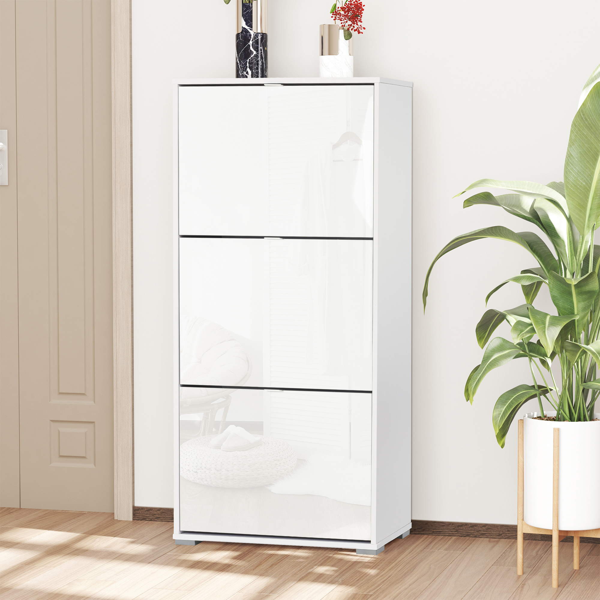 Un zapatero blanco con tres cajones abatibles junto a una puerta y una planta.