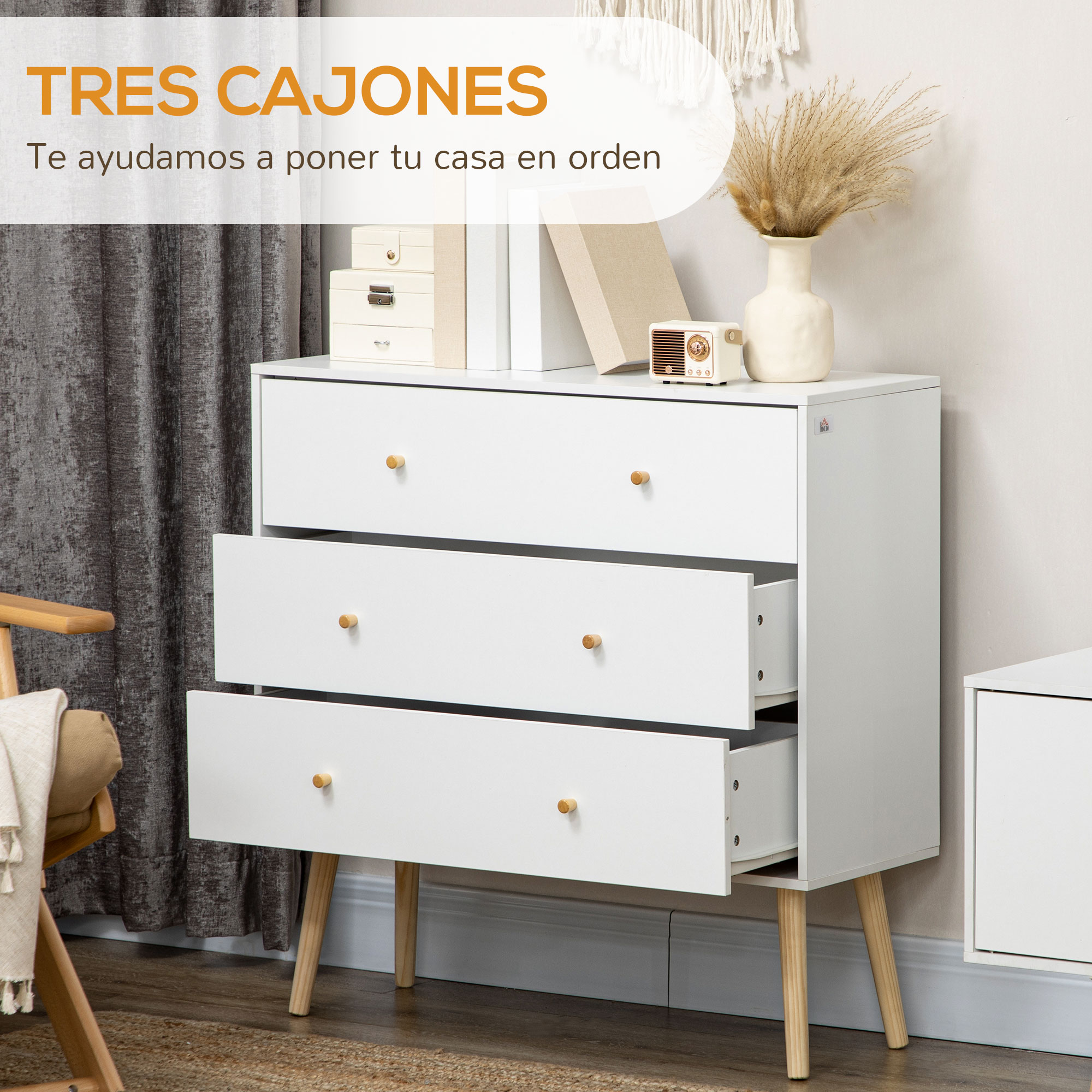 Cómoda blanca de tres cajones con patas de madera junto a un sillón.