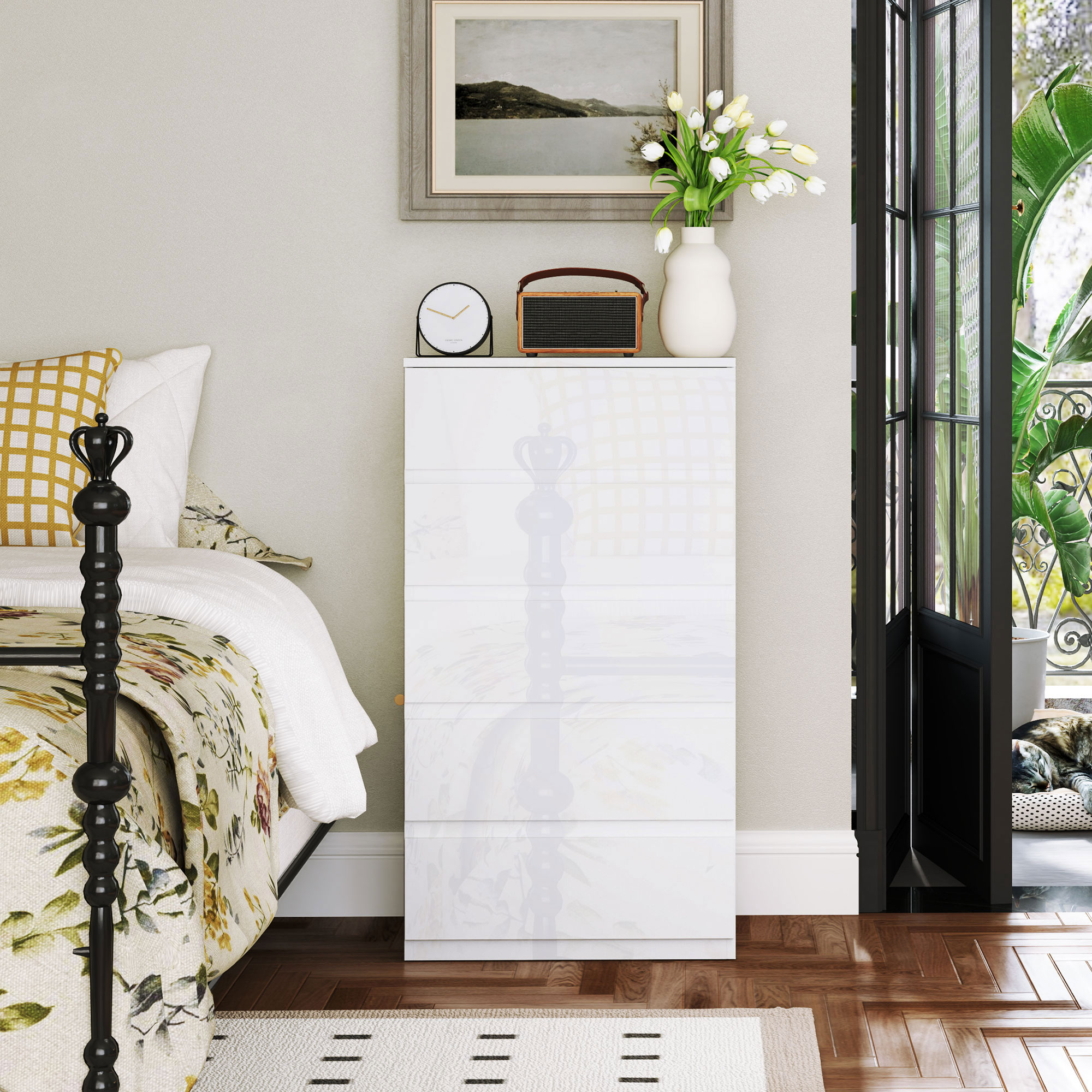 Una cómoda blanca junto a una cama floral. Una ventana con plantas al fondo.