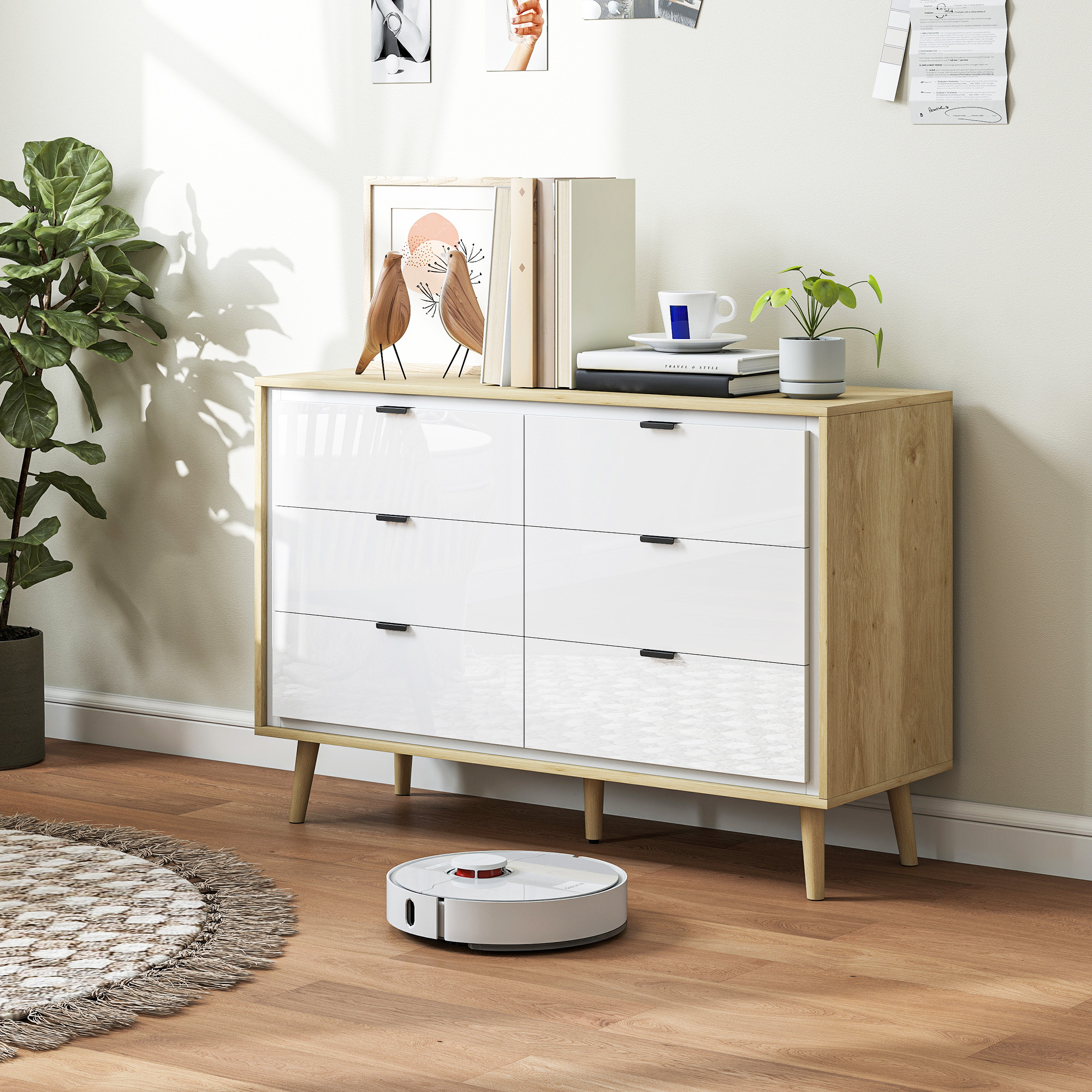Un robot aspirador blanco limpia un suelo de madera junto a una cómoda de seis cajones blancos.