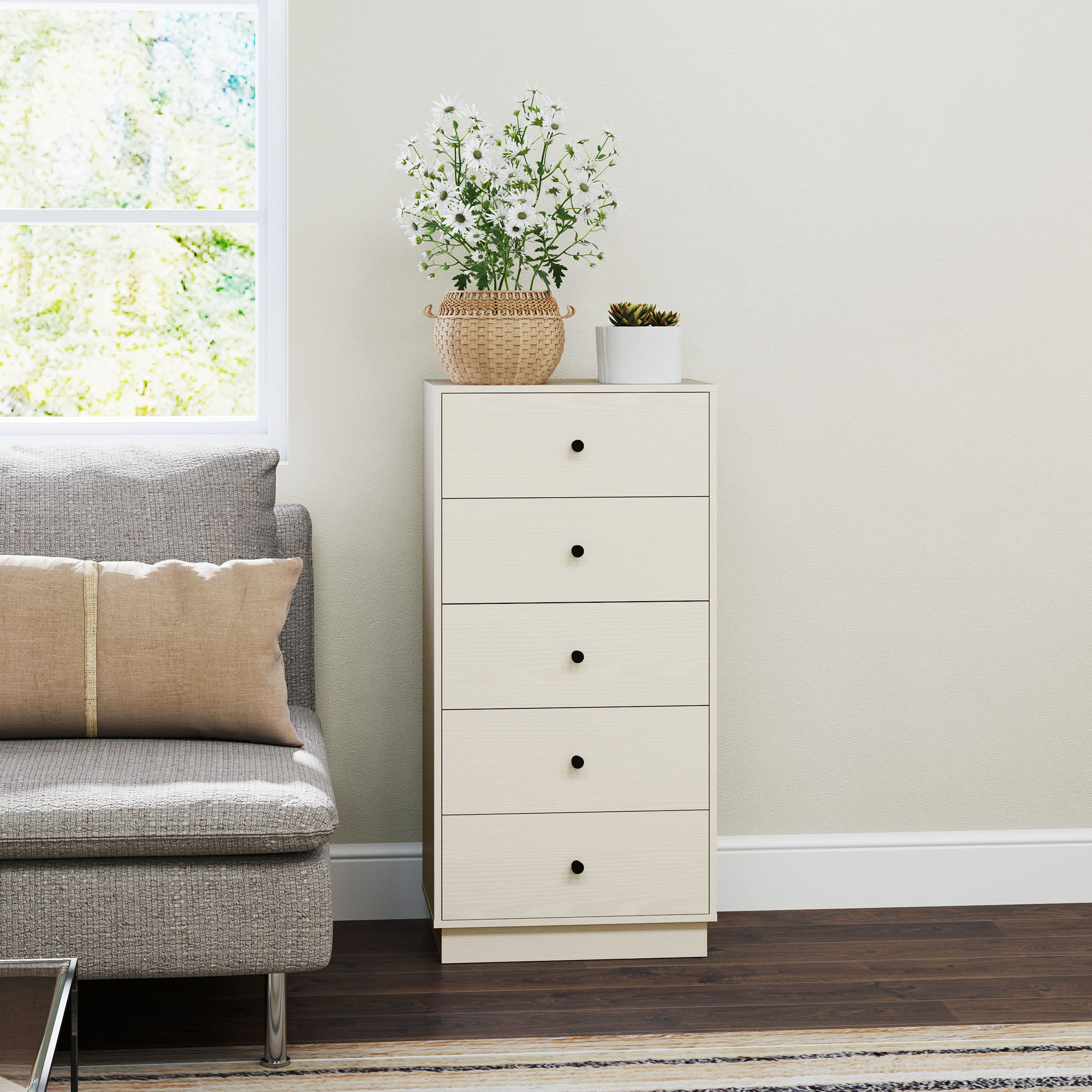 Una cómoda de madera clara con pomos negros se sienta junto a un sofá gris con un cojín beige.