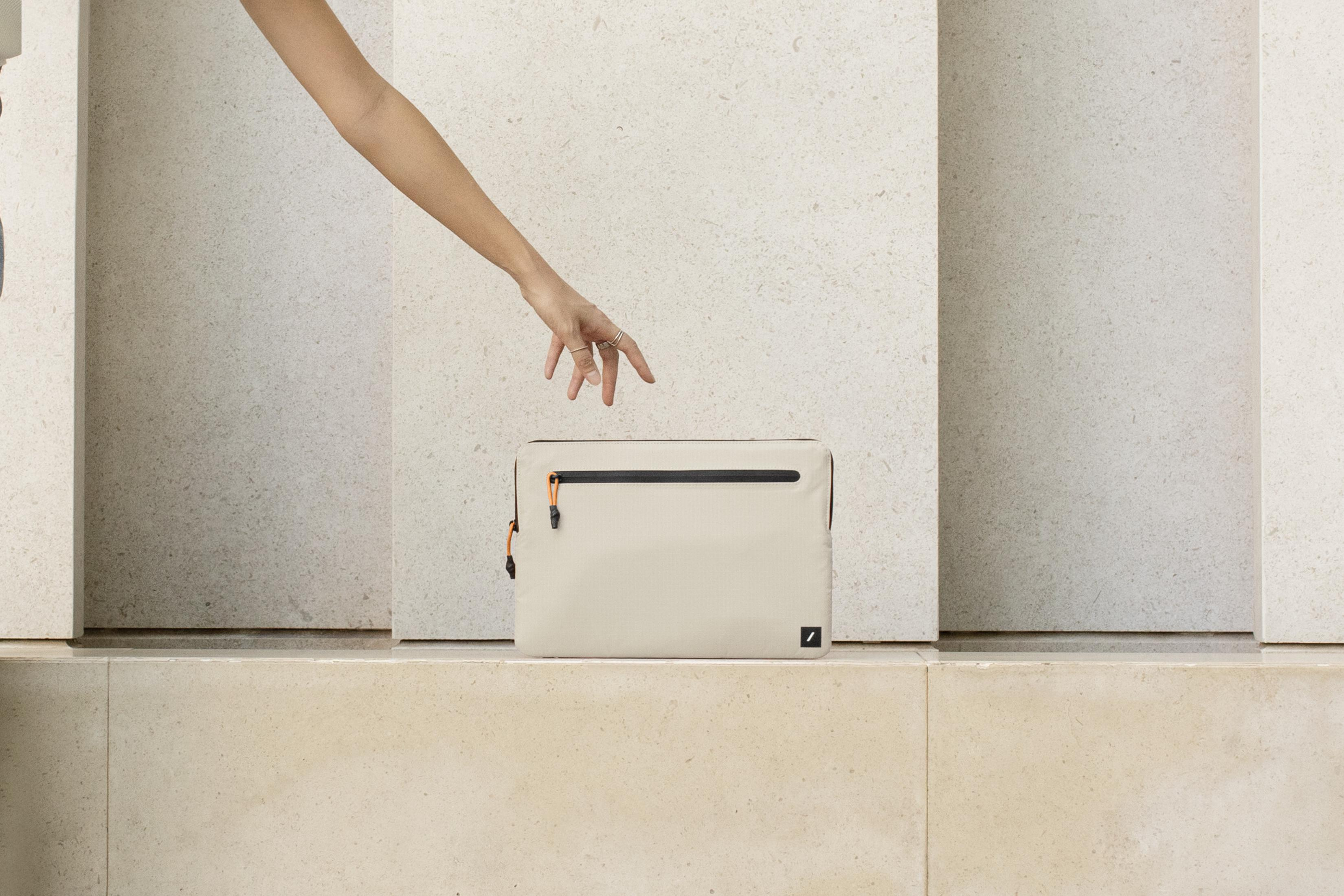 Una mano raggiunge una borsa beige chiaro con tiretti arancioni.