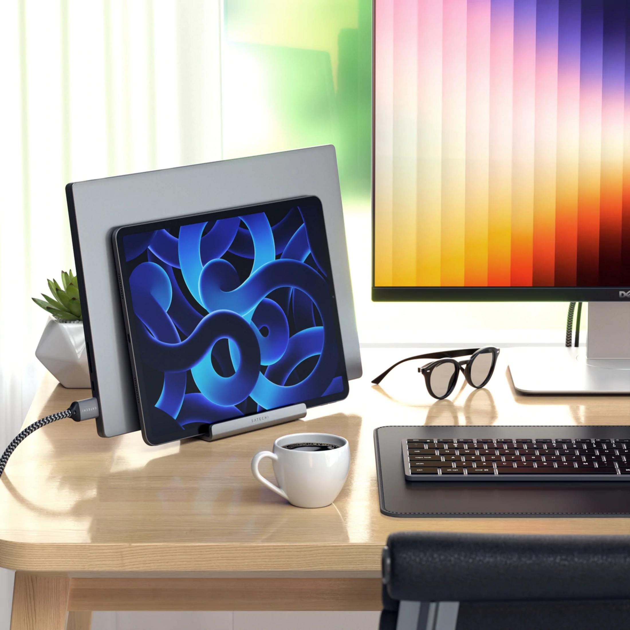 Una scrivania con tablet, monitor, caffè e tastiera.