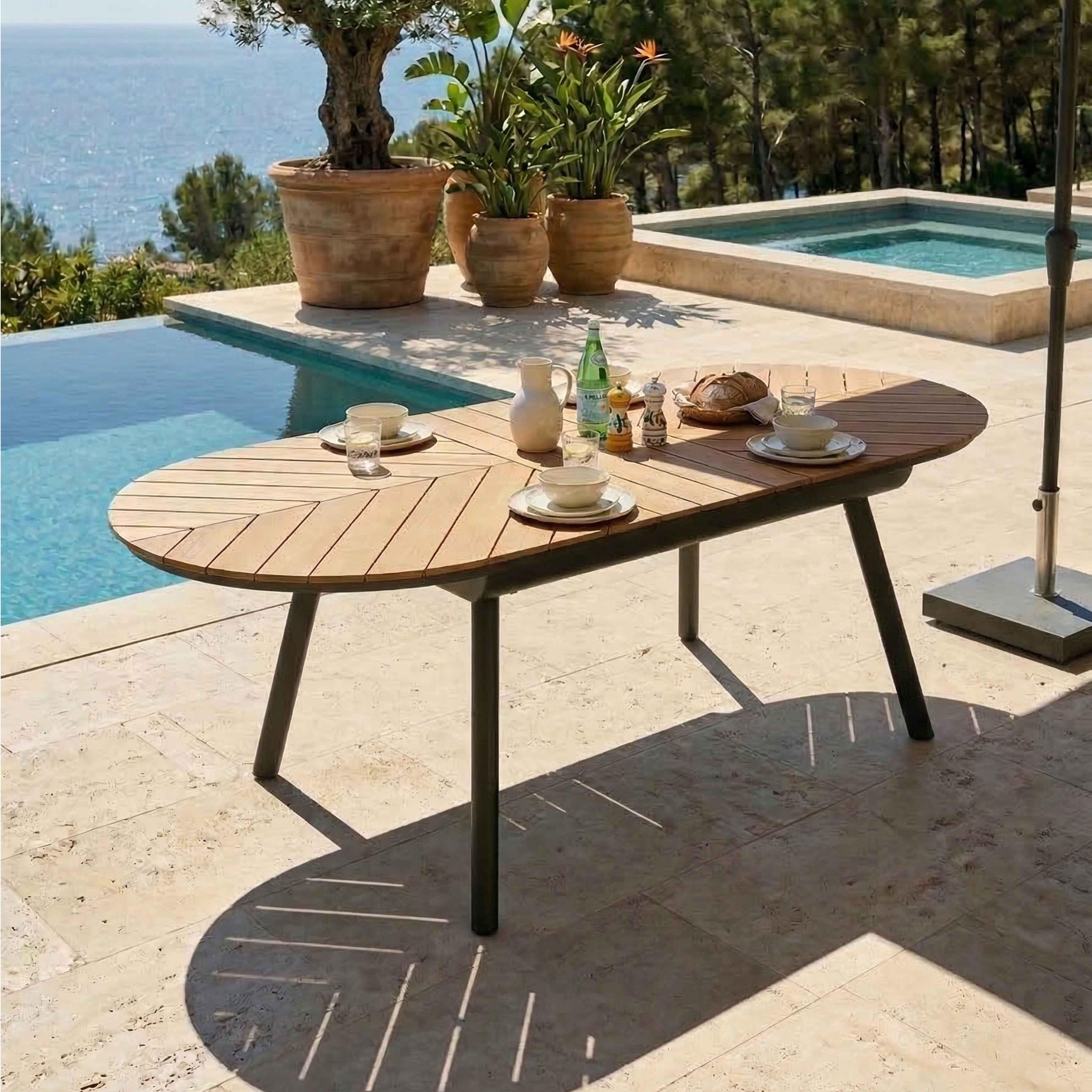 Ein ovaler Holztisch mit Geschirr steht auf einer Terrasse am Pool.
