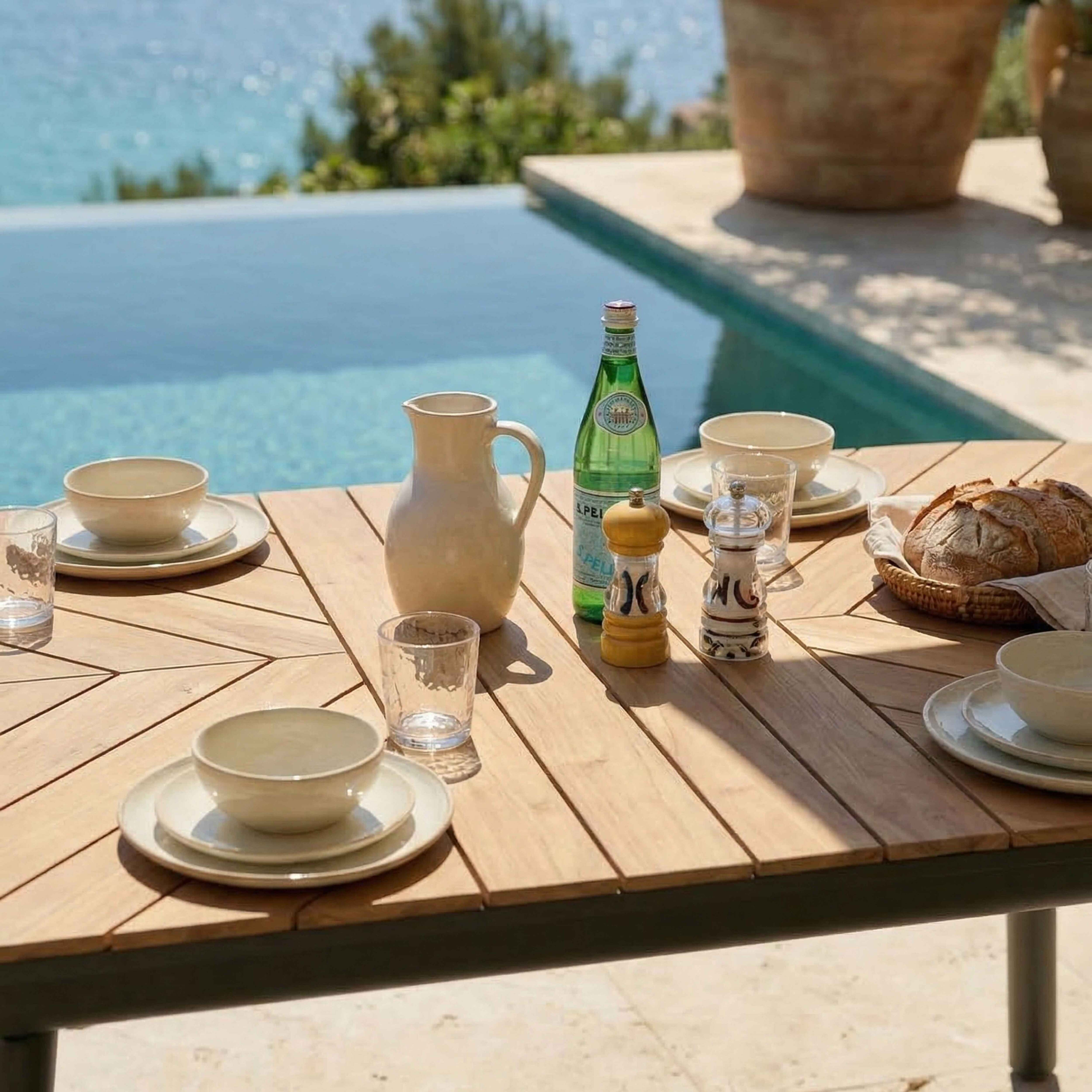 Holztisch mit Geschirr, Brot und Wasserflasche am Pool.