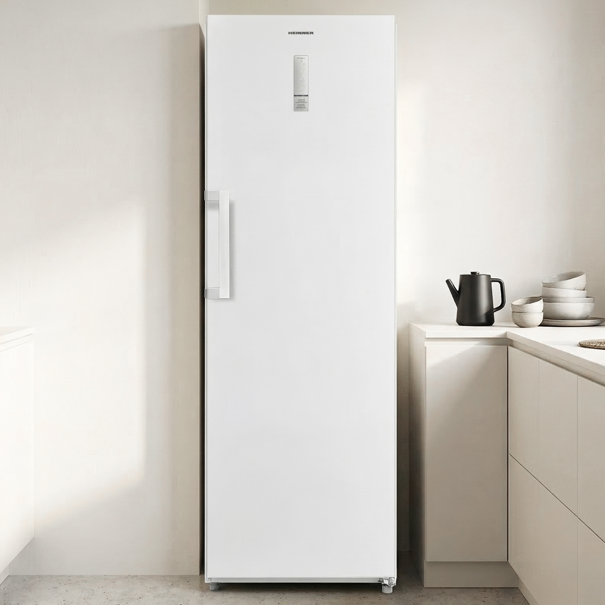 Ein schlanker weißer Kühlschrank steht neben einer Küchenzeile mit schwarzem Wasserkocher.