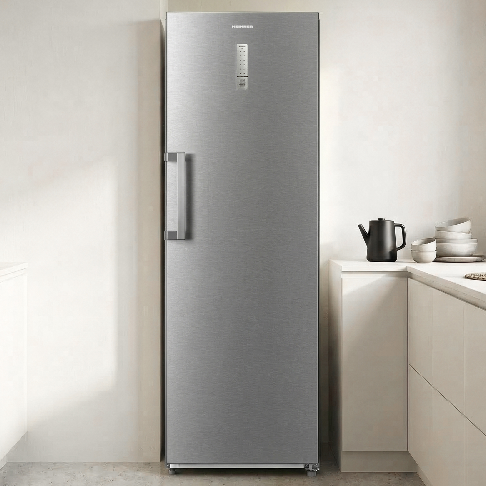Ein schlanker, silberner Kühlschrank steht neben einer Küchenzeile mit schwarzem Wasserkocher.