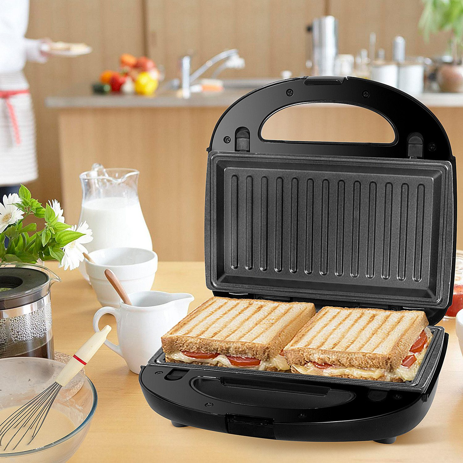 Offener Sandwichmaker mit zwei gegrillten Sandwiches. Küchentheke mit Milchkrug, Schneebesen und Schüssel.