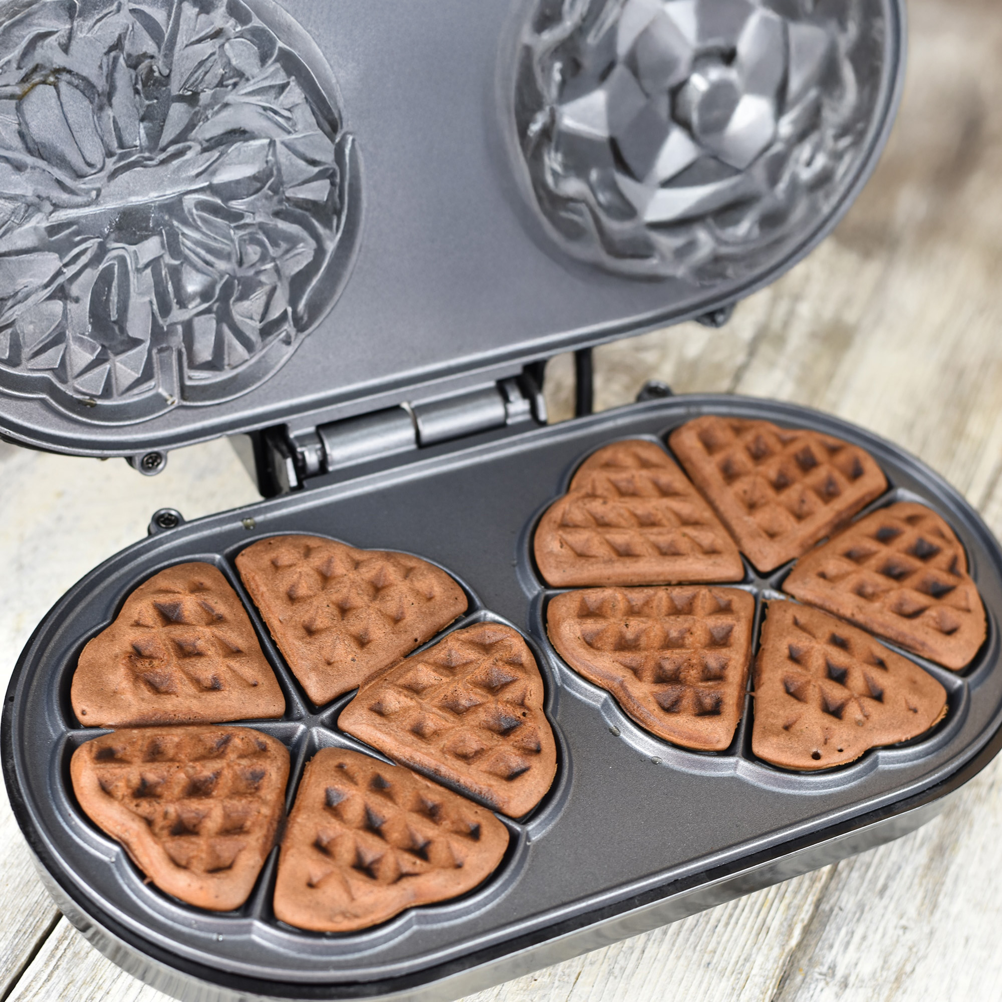 An open waffle maker with cooked heart-shaped waffles inside.