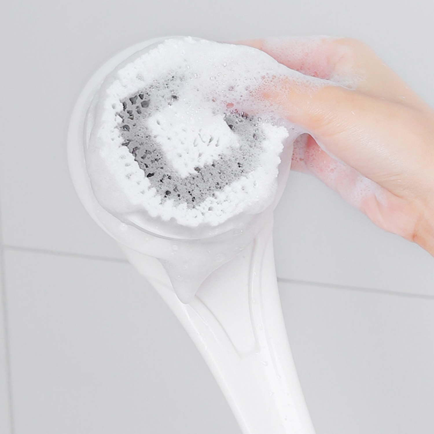 Hand mit Seife schäumt elektrischen Gesichtsreiniger im Badezimmer.