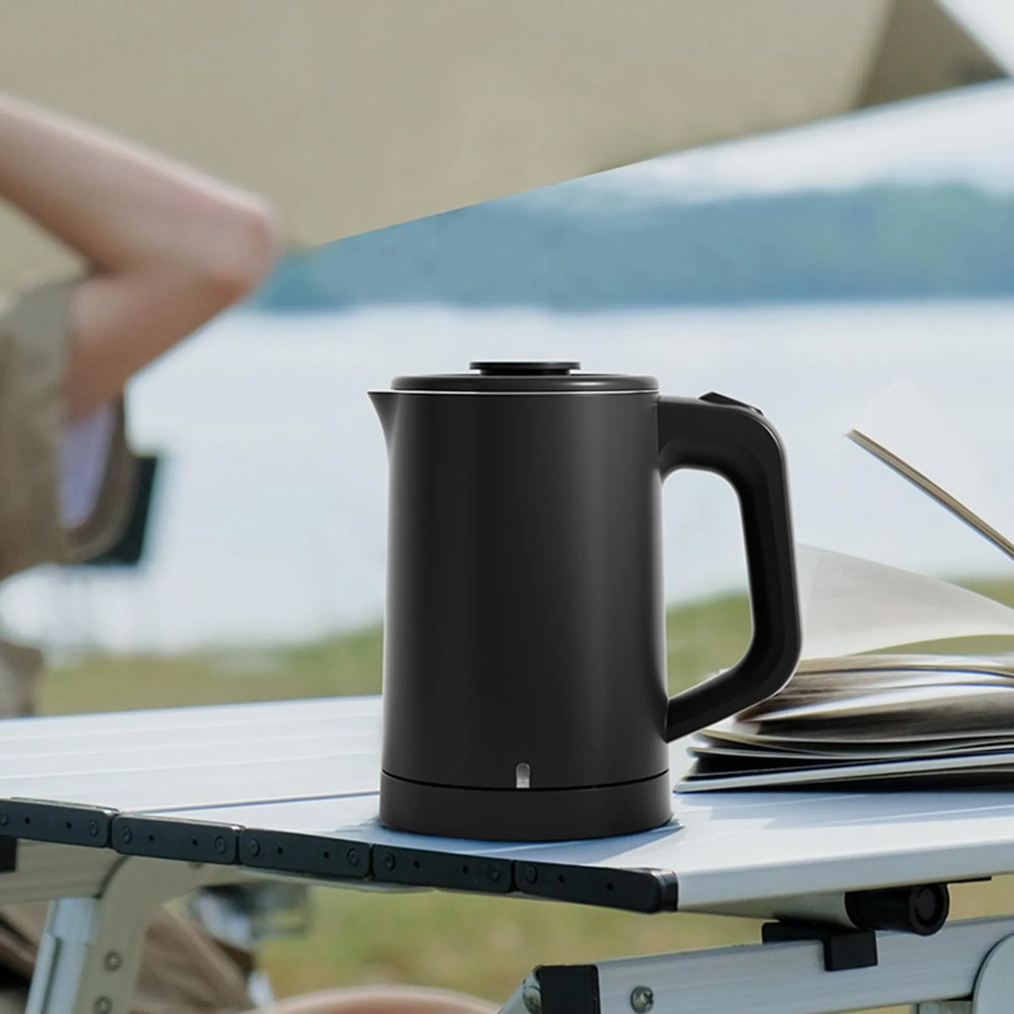 Schwarzer Wasserkocher auf Tisch mit Büchern und Landschaft im Hintergrund.
