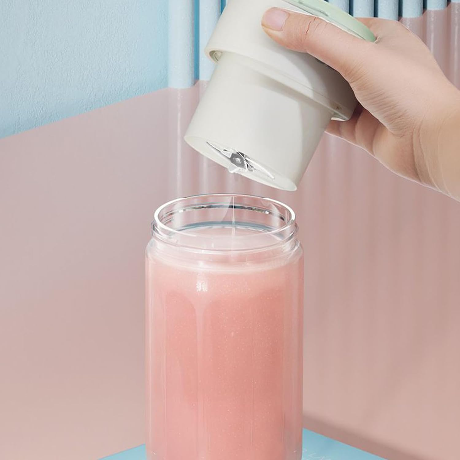 Eine Hand hält einen Mixeraufsatz über ein Glas mit rosa Flüssigkeit.
