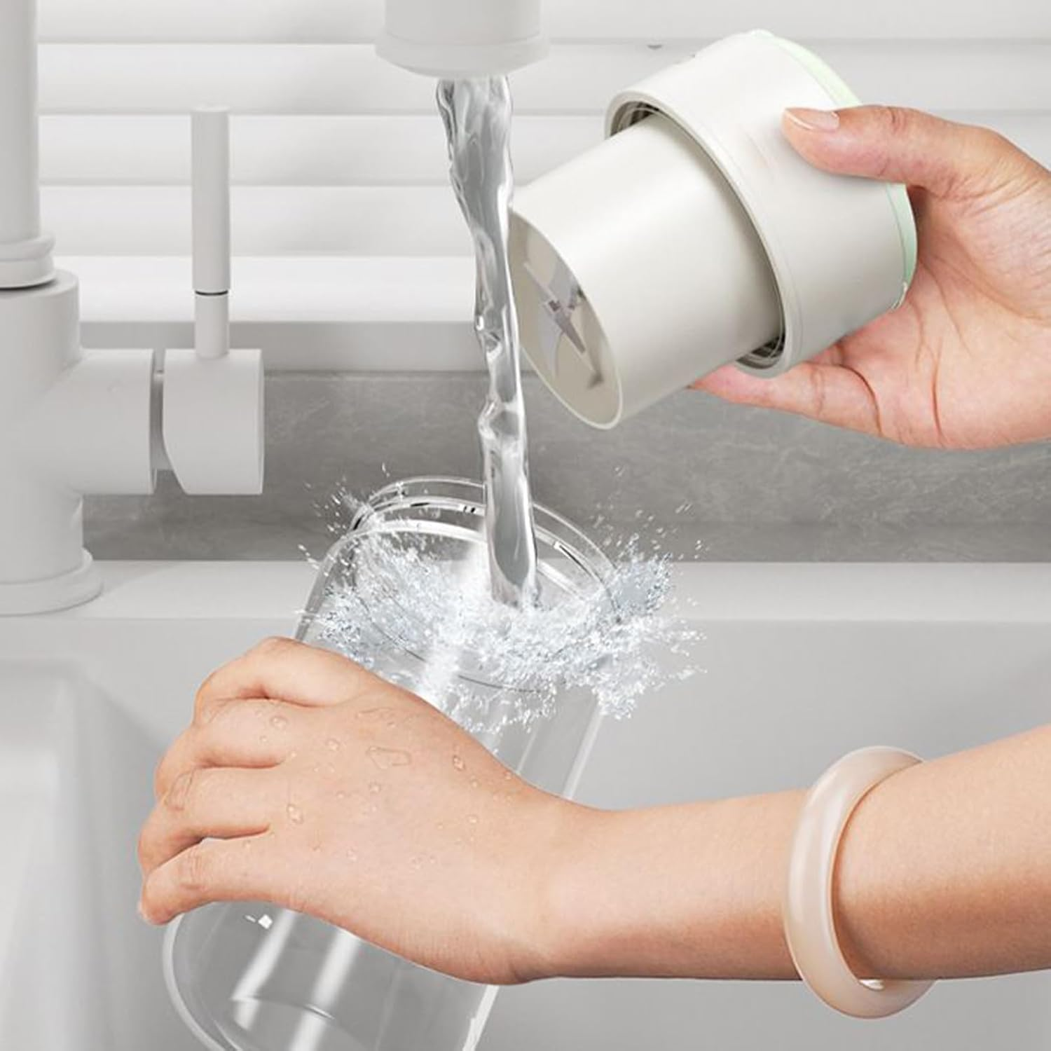 Eine Hand hält einen Mixeraufsatz unter fließendes Wasser in einem Glas.