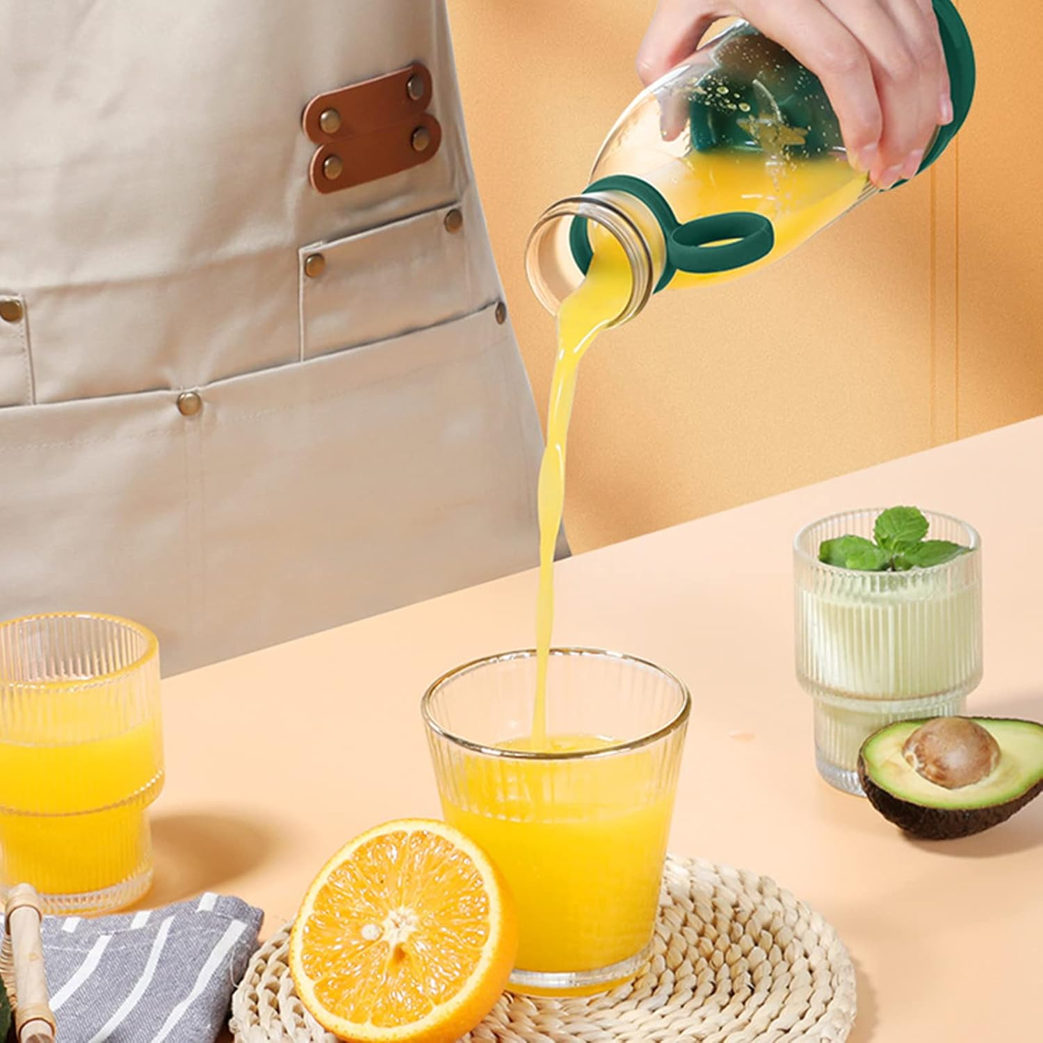 Eine Hand gießt Orangensaft aus einer Flasche in ein Glas. Eine halbe Orange liegt daneben.