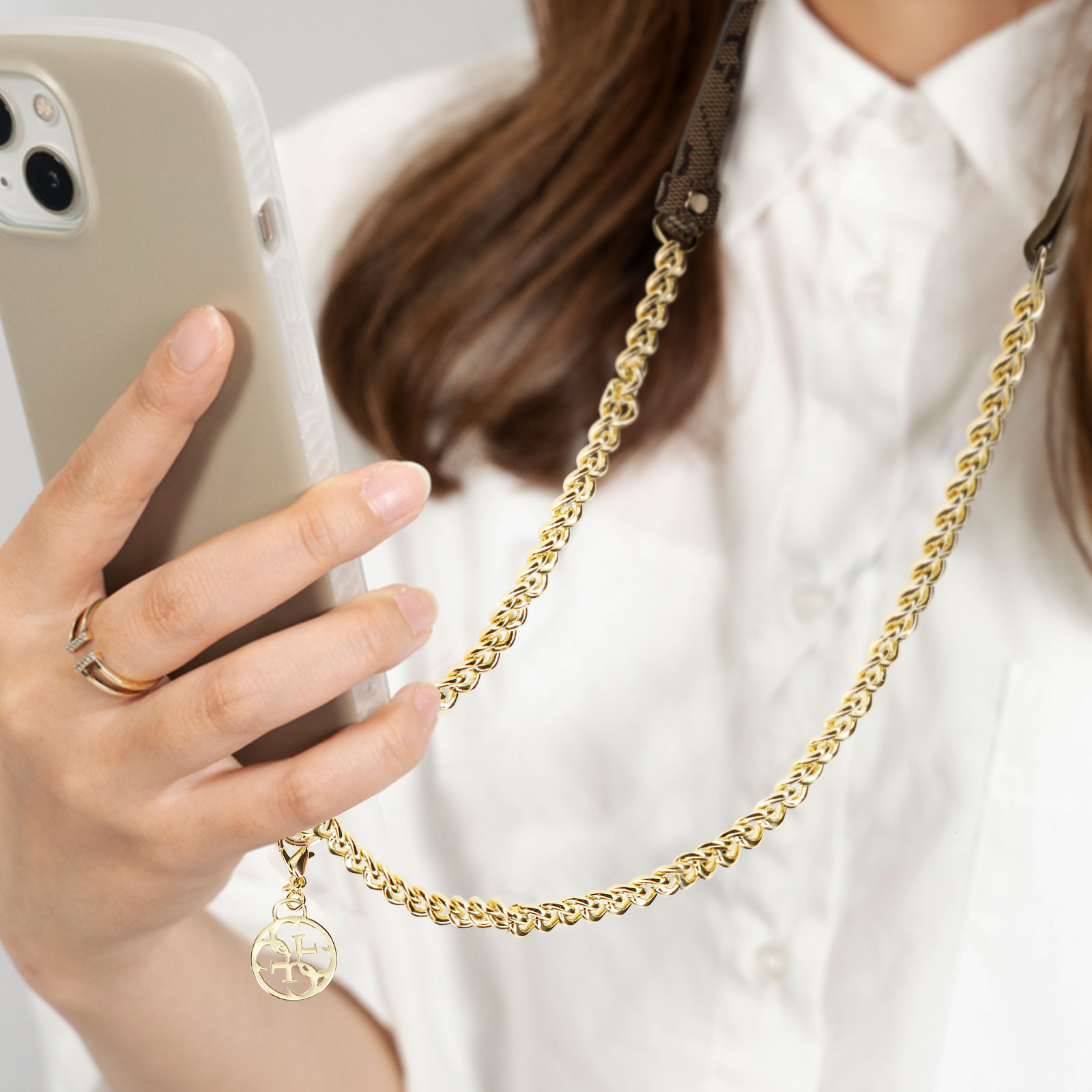 Eine Hand mit Ring hält ein Handy, daran eine goldene Kette mit Anhänger.