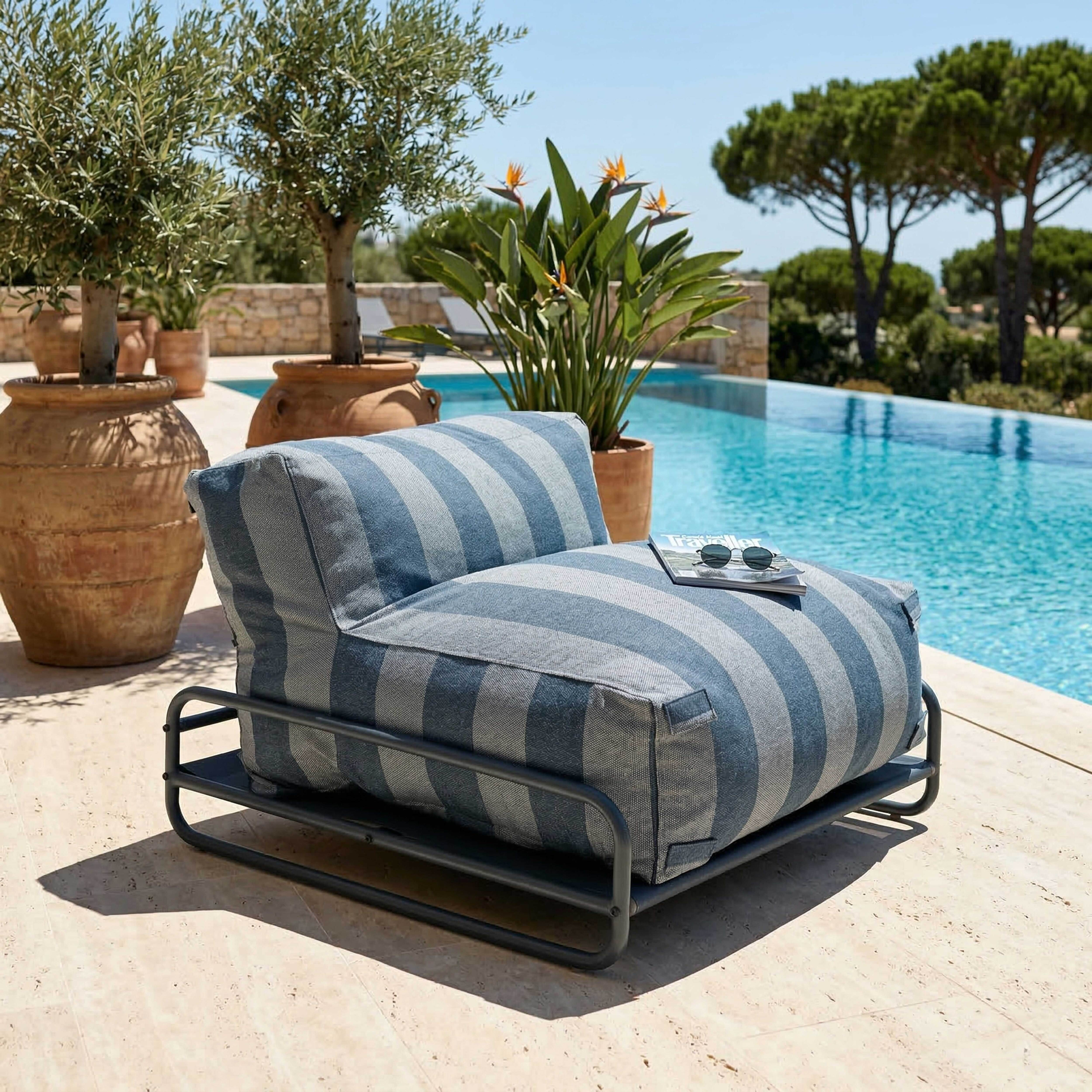 Ein gestreifter Sessel am Pool mit Olivenbäumen und Palmen im Hintergrund.