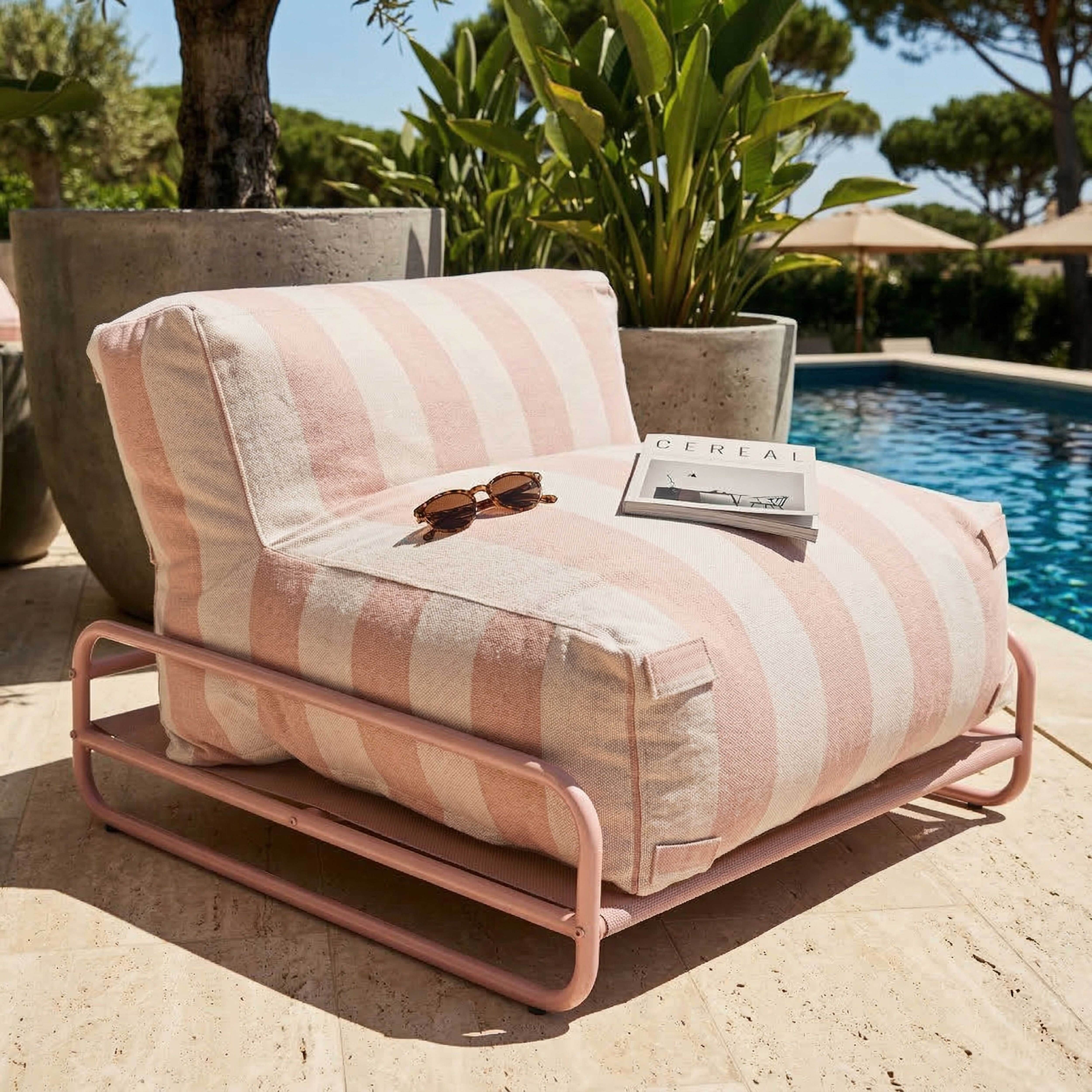 Ein gestreifter Sessel mit Sonnenbrille und Zeitschrift neben einem Pool.