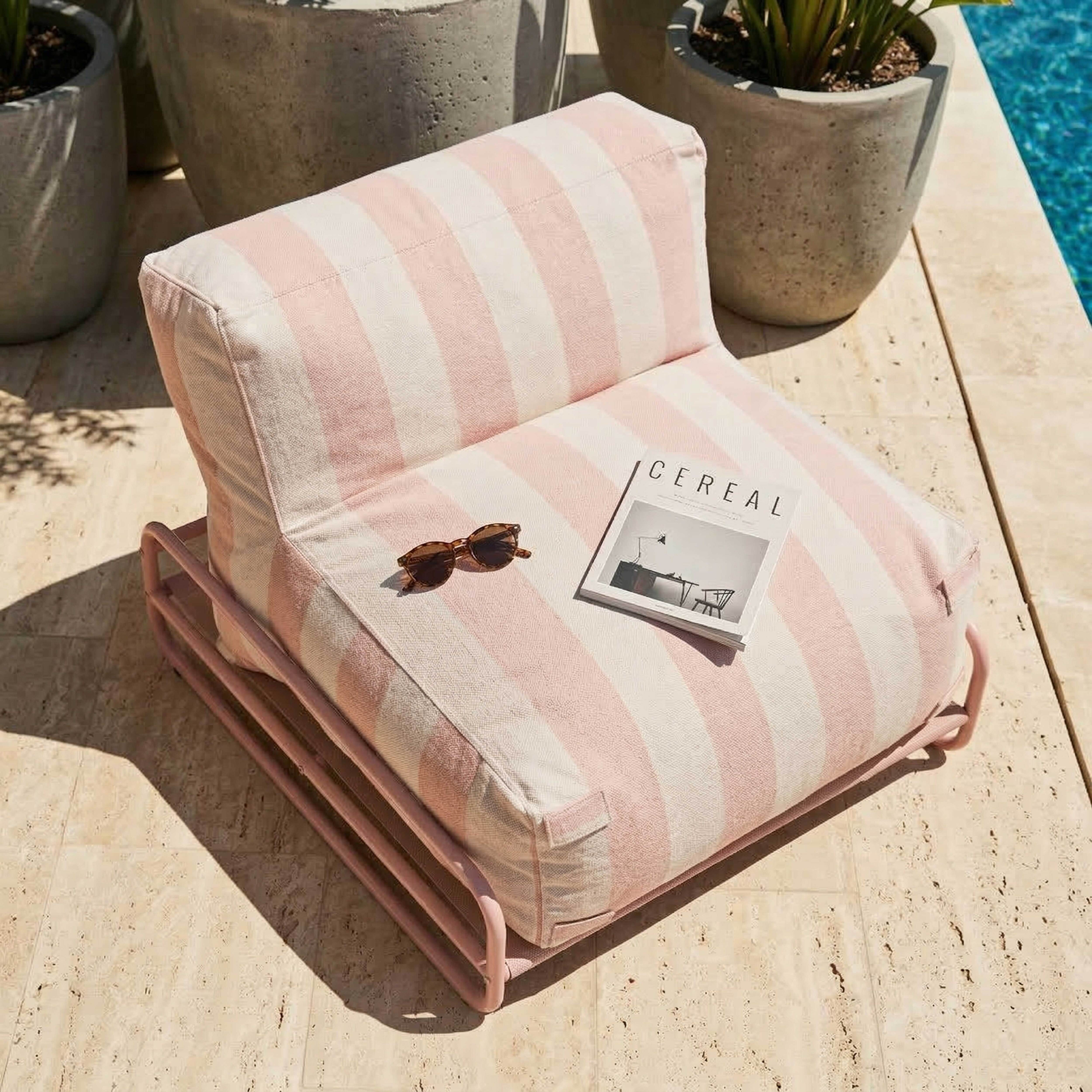 Ein gestreifter Sessel mit Sonnenbrille und Zeitschrift neben einem Pool.