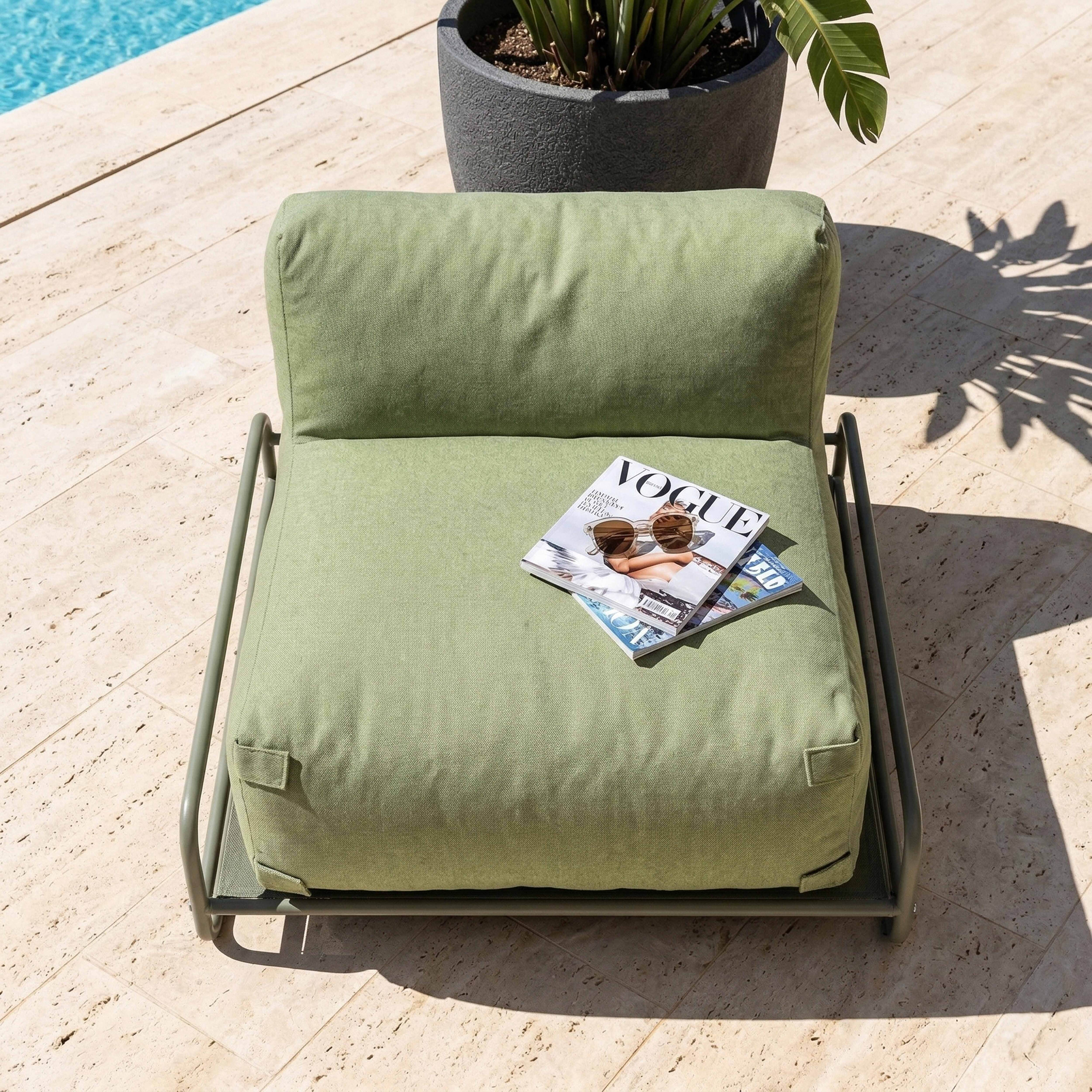 Ein grüner Sessel steht auf einer Steinplatte neben einem Pool. Ein Magazin liegt darauf.