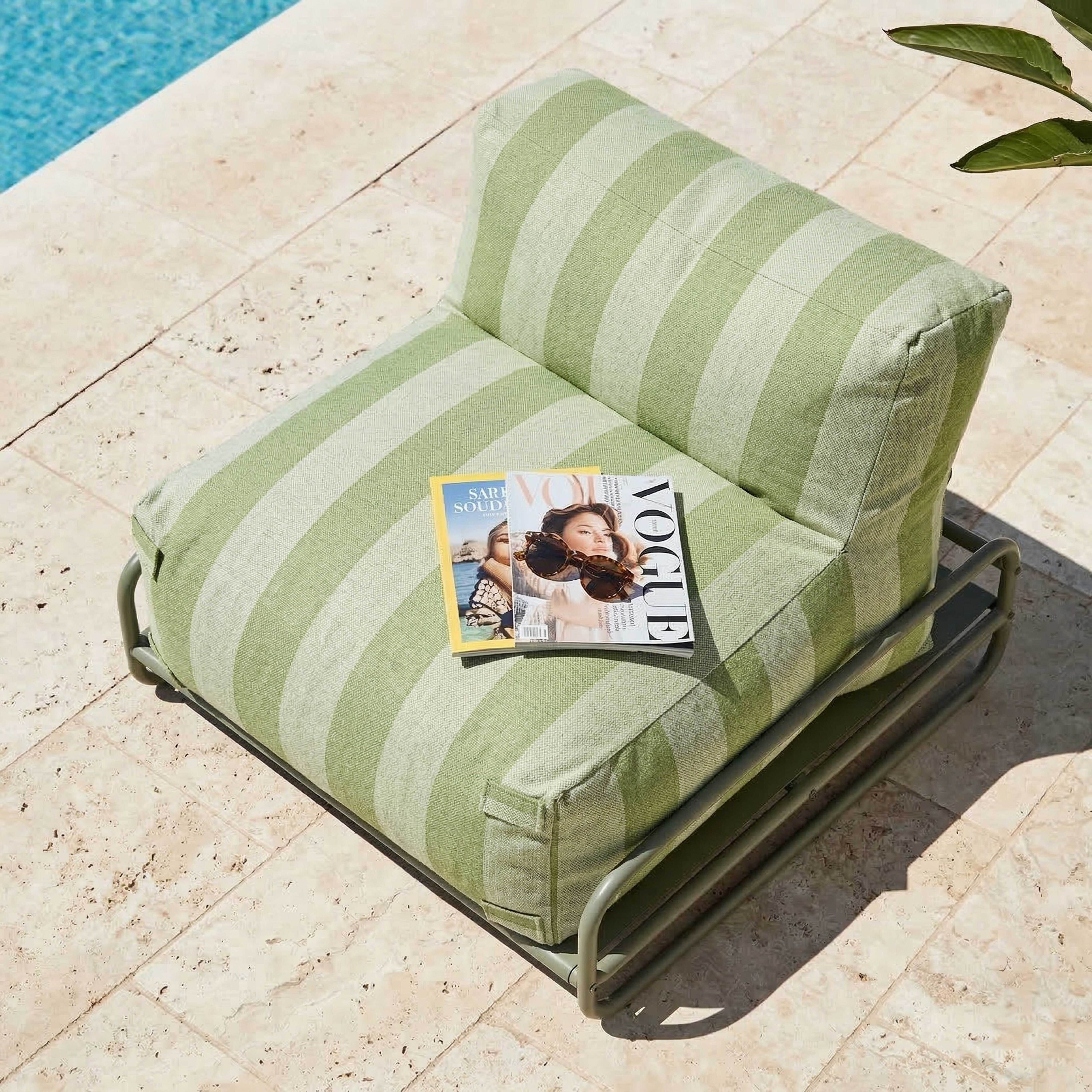 Ein gestreifter Sessel neben einem Pool mit zwei Magazinen und Sonnenbrillen darauf.