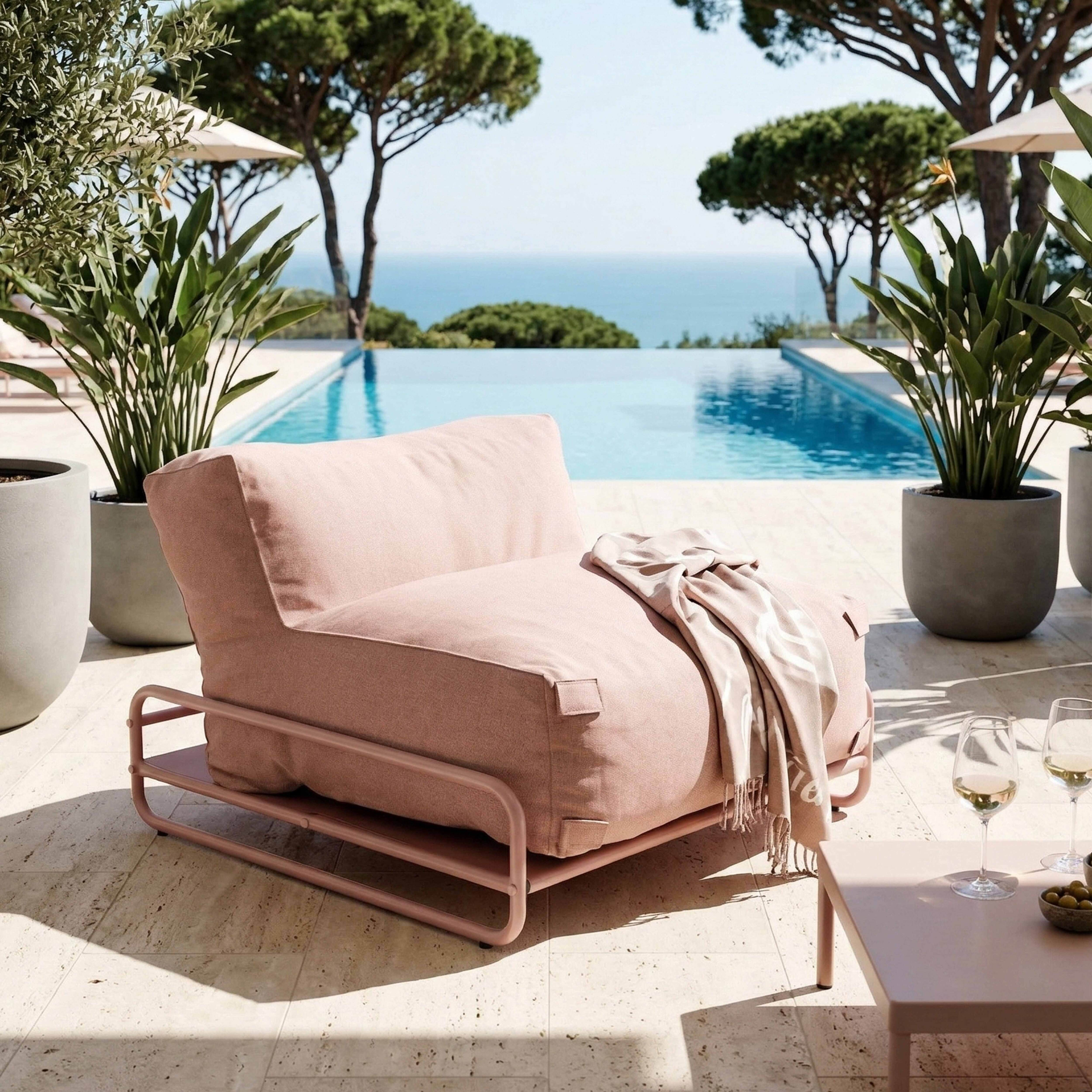 Ein rosa Sessel mit Decke steht an einem Pool mit Blick auf das Meer.