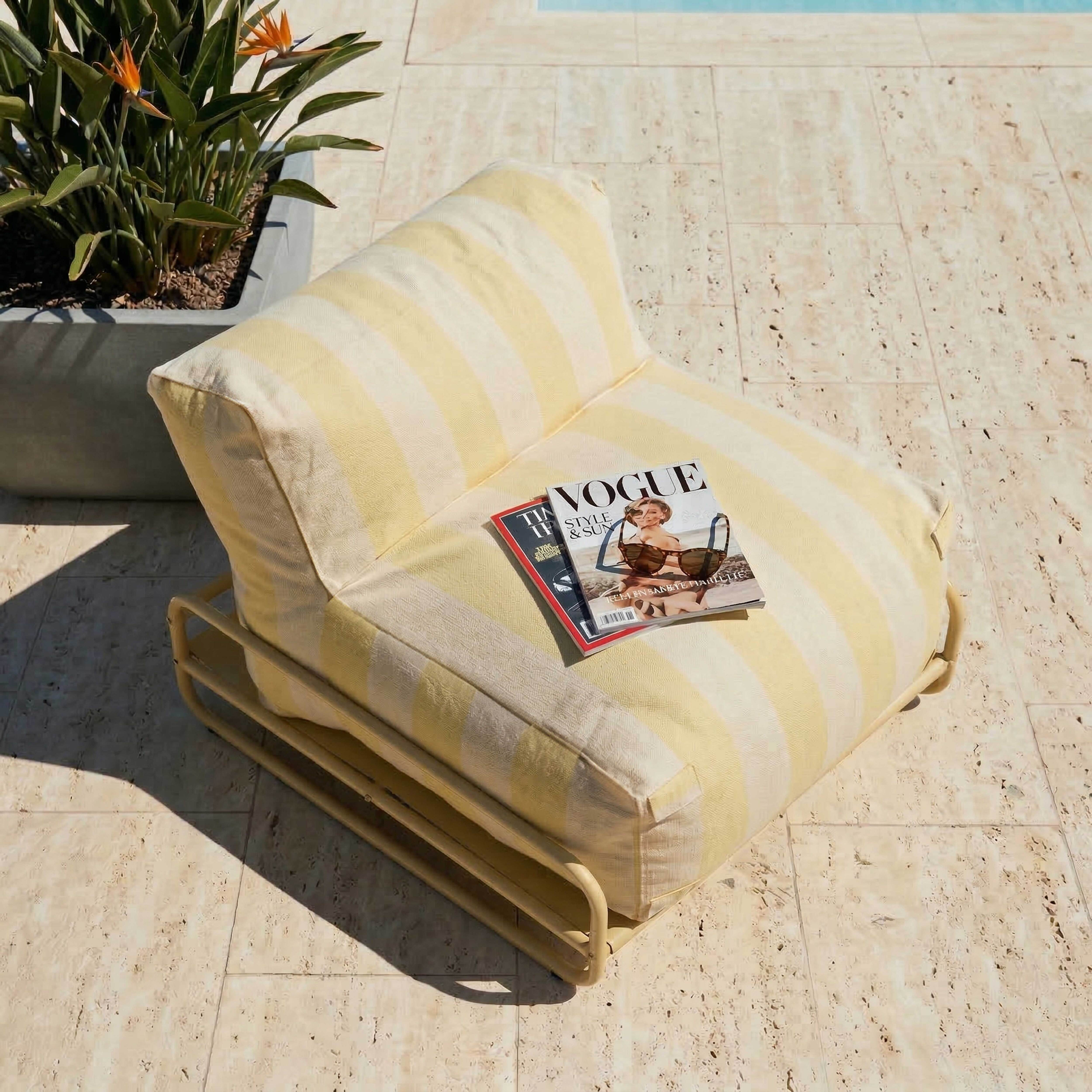 Ein gestreifter Sessel neben einem Pool mit einem Vogue-Magazin.