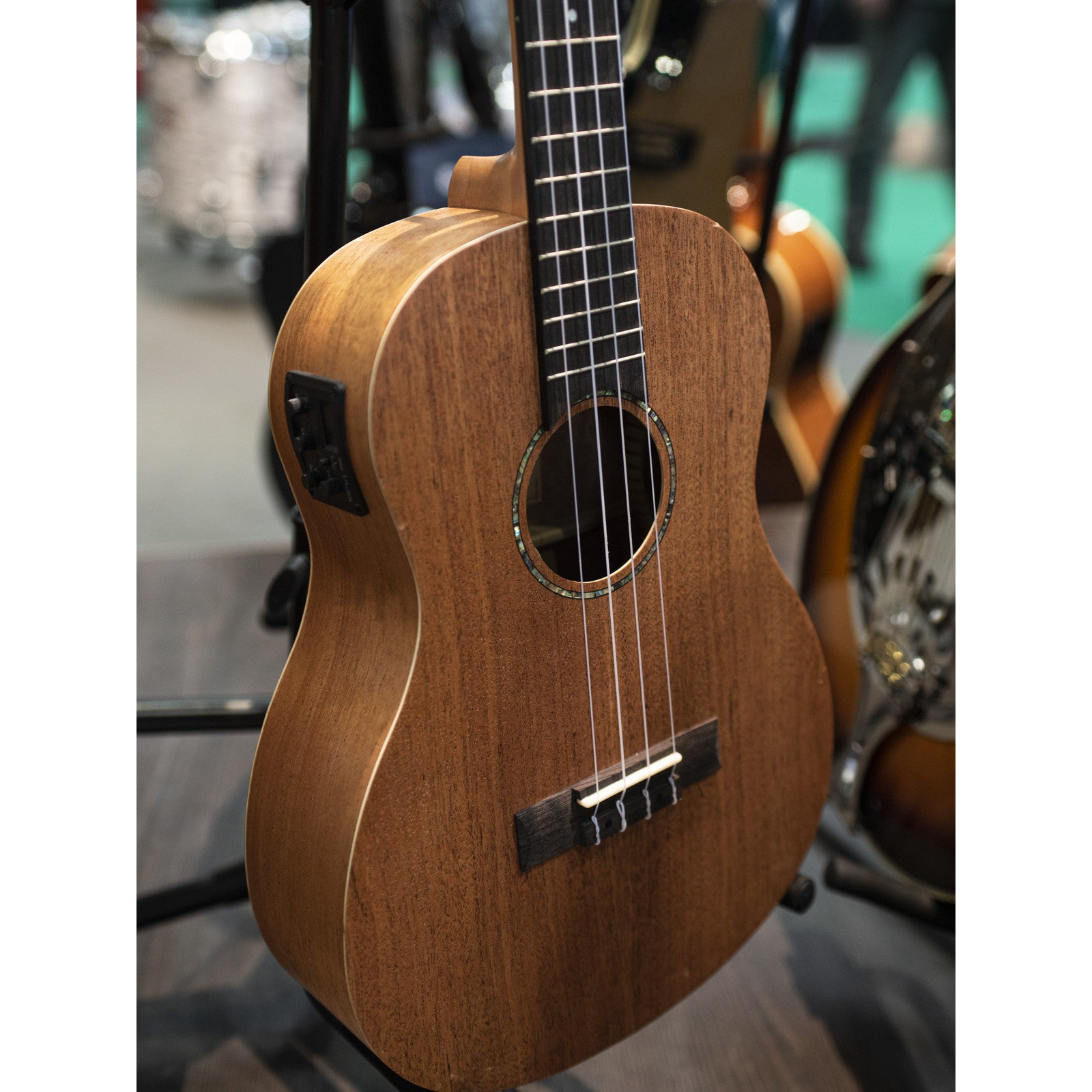 Een bruine ukulele met vier snaren en een zwart toetsenbord staat op een standaard.