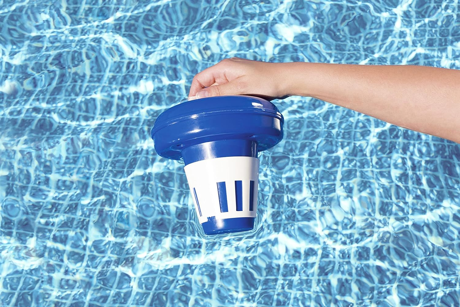 Eine Hand legt einen blauen und weißen Pool-Chemikalien-Spender in klares blaues Wasser.